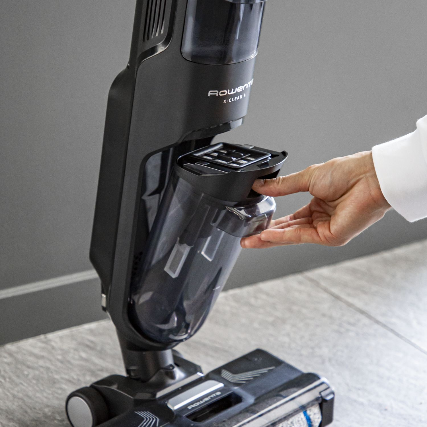 A black Rowenta vacuum cleaner. A hand is opening the dust container.