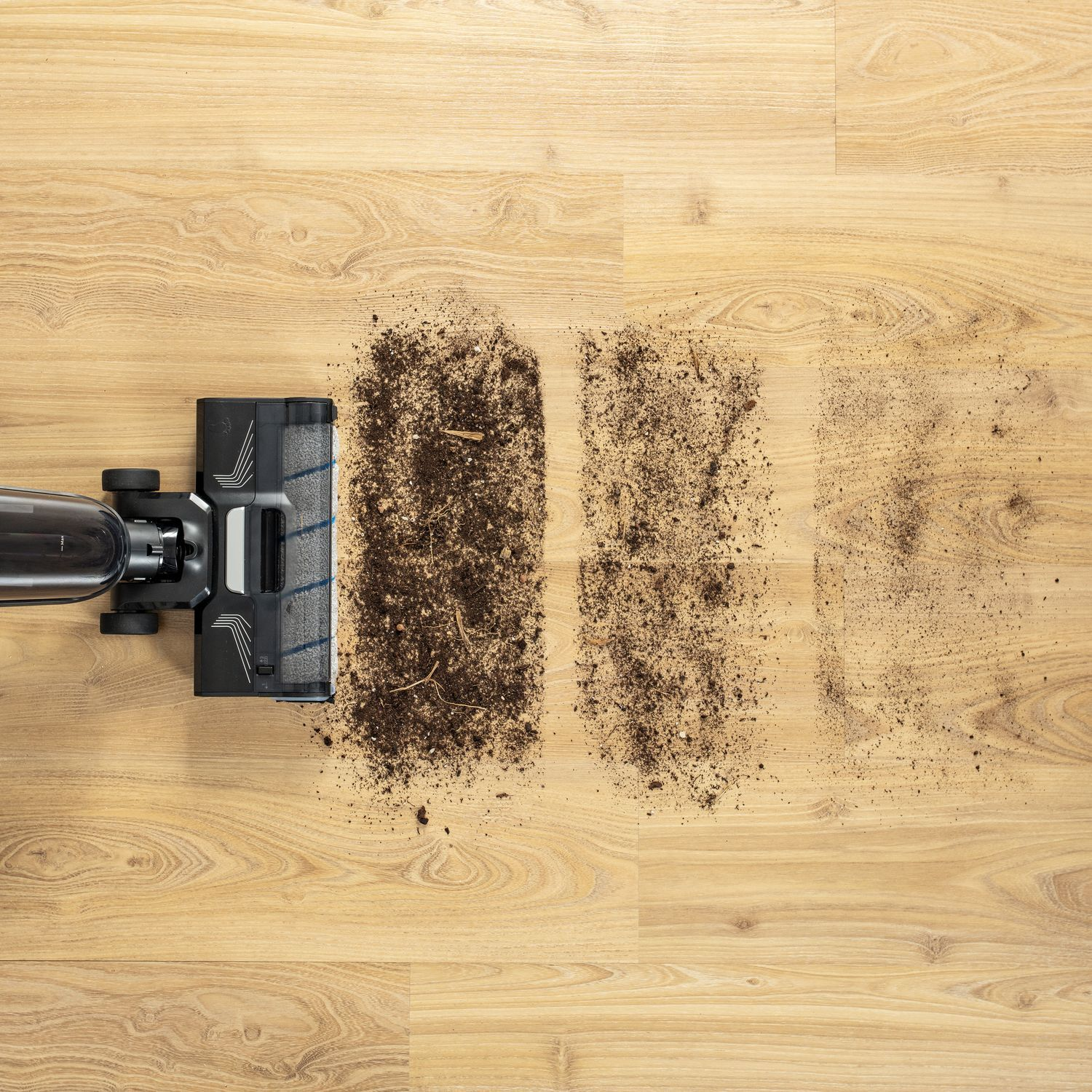 Vacuum cleaner on wooden floor cleaning dirt, showing a cleaned line and a dirty line.