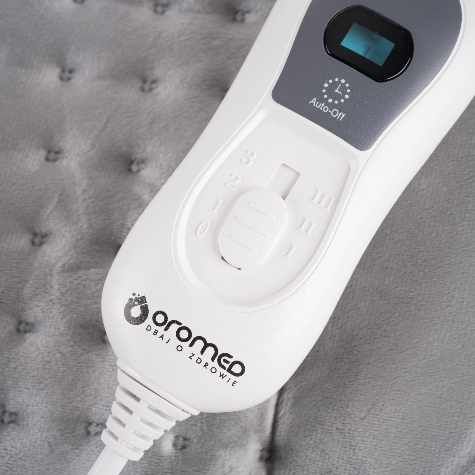 Biały i szary panel sterowania elektrycznej poduszki grzewczej, z numerami i przyciskiem.