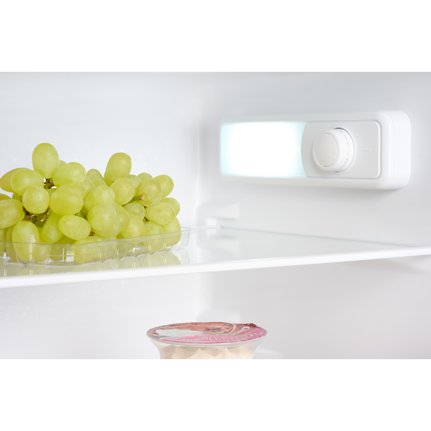Grapes in a container, a light, and a dial inside of a refrigerator.