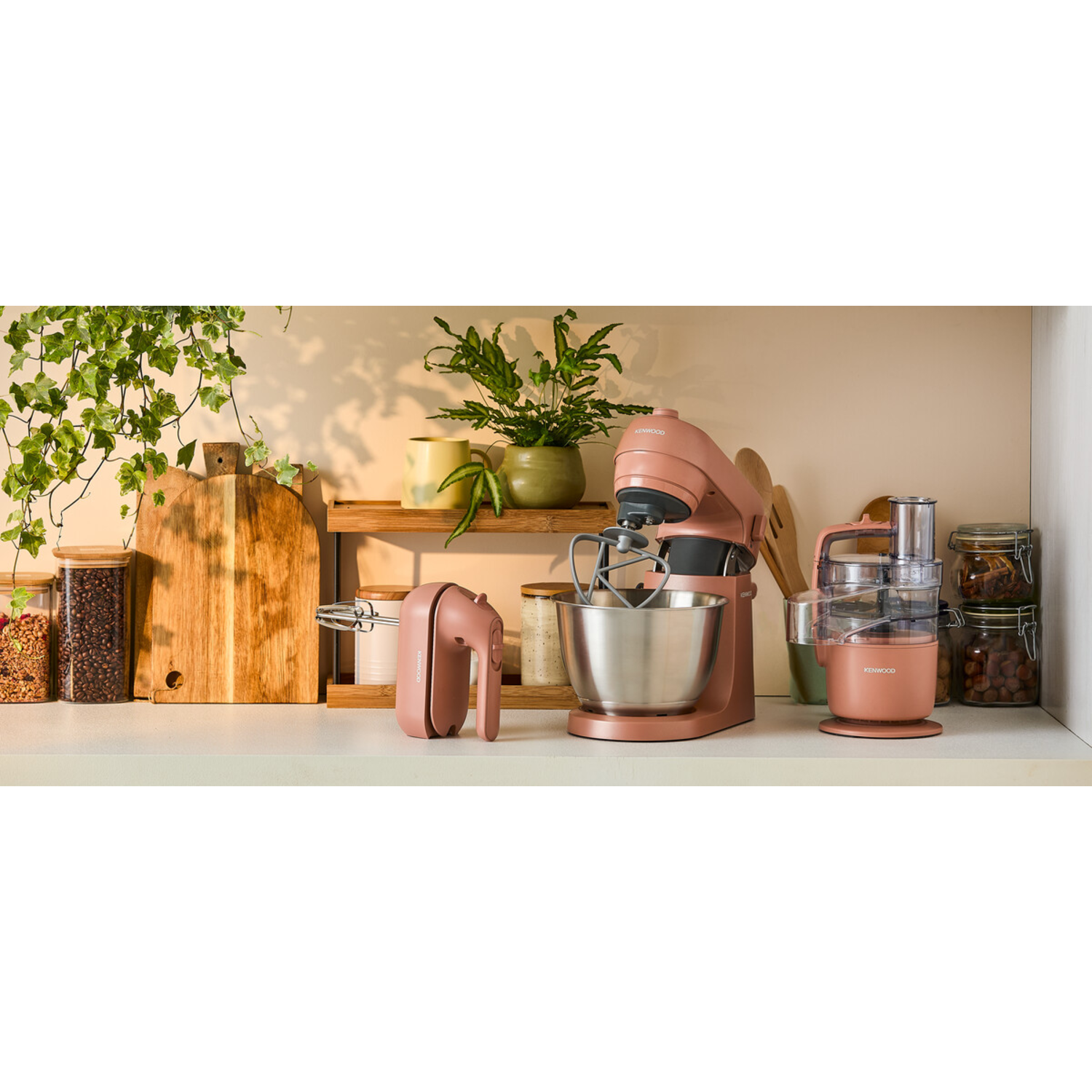 A kitchen shelf with a pink mixer, hand mixer, and food processor with wooden cutting boards.