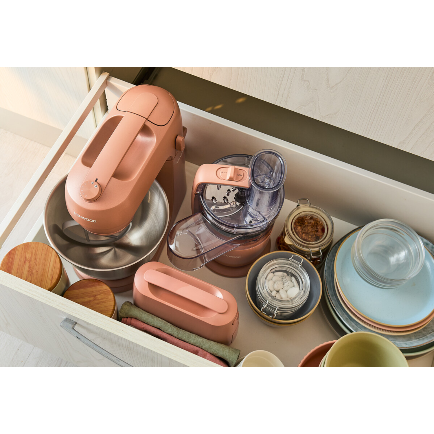 A drawer filled with kitchen appliances and tools: a mixer, a food processor, and jars.