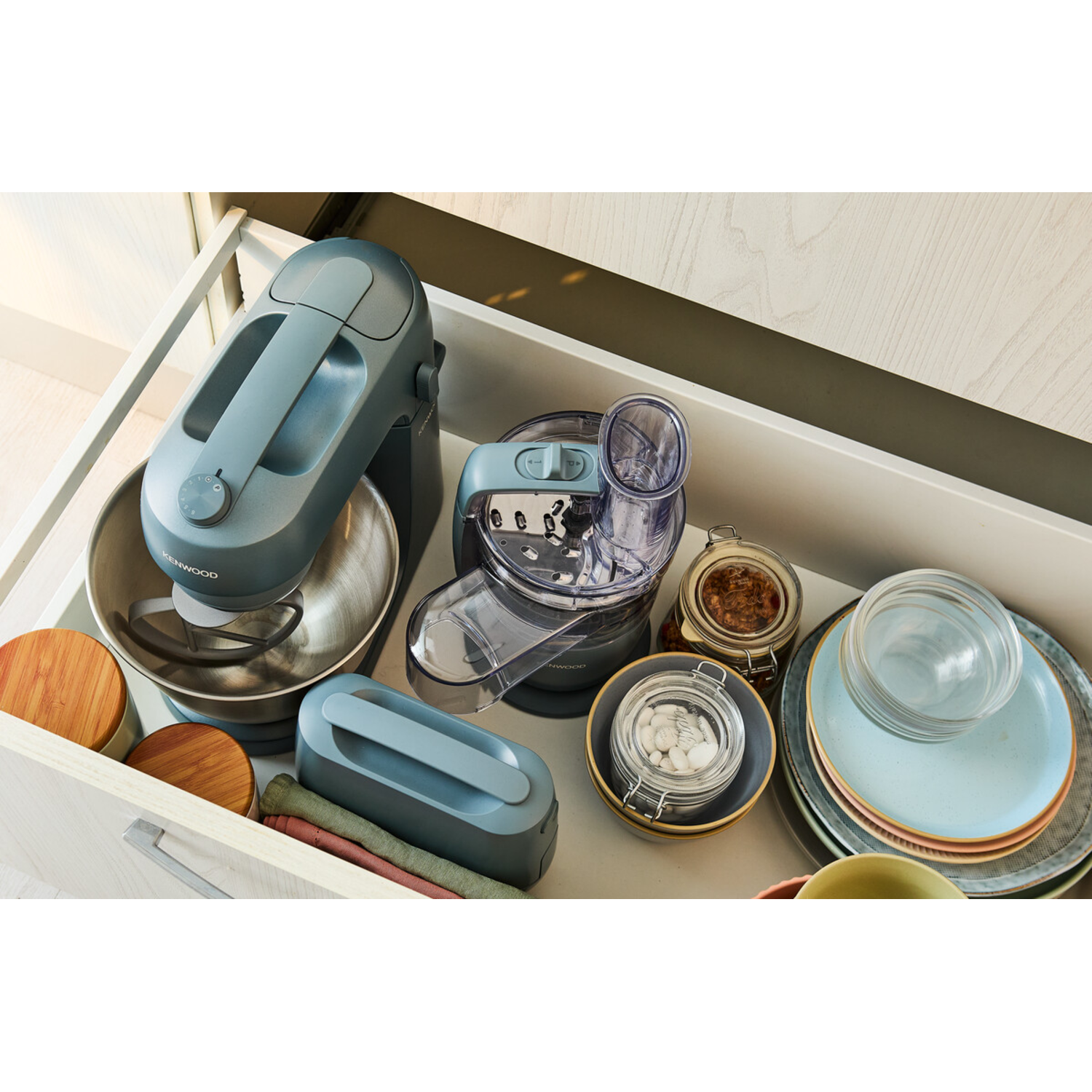 Open keukenkast, met mixer, keukenmachine, borden, potten en accessoires.