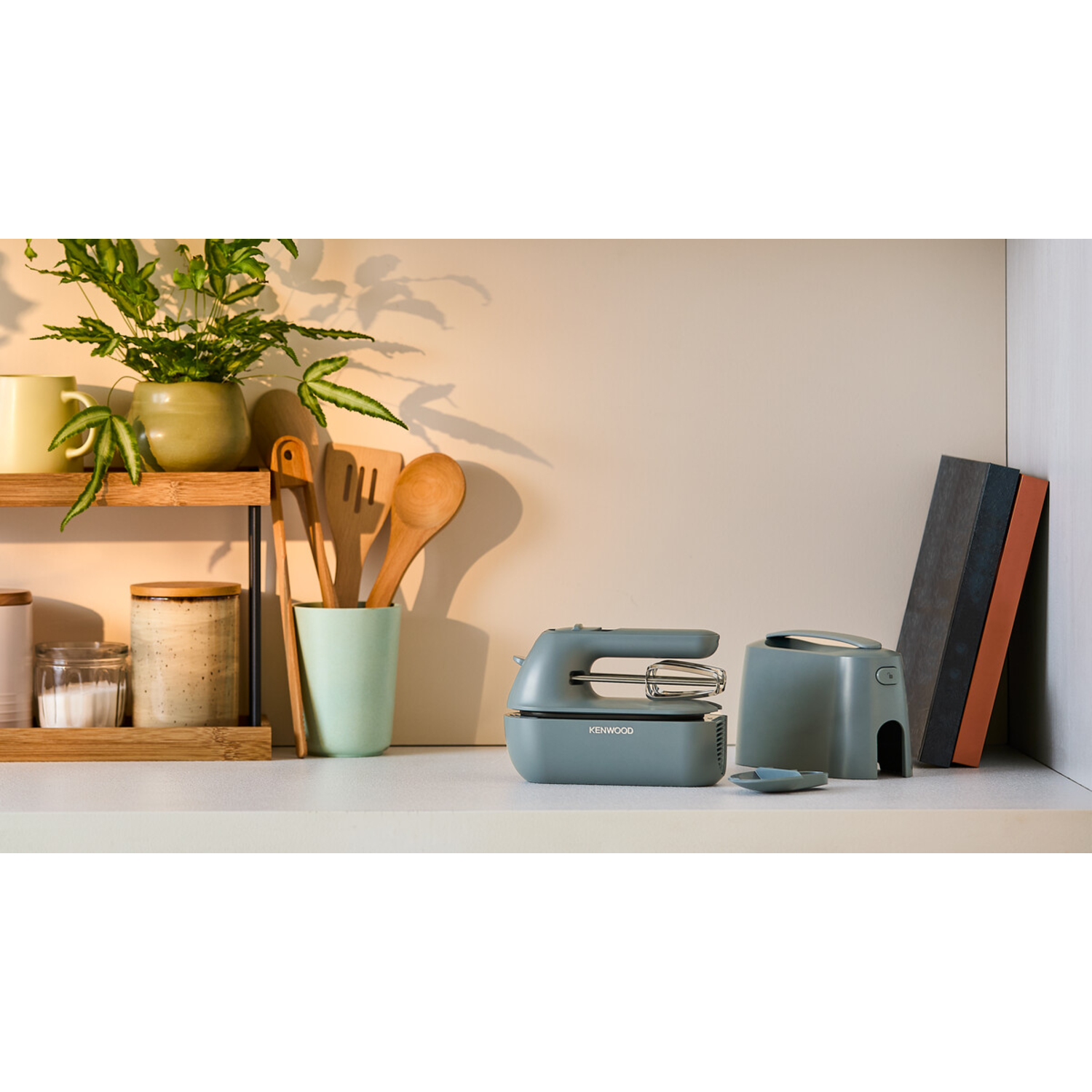 A kitchen counter with a mixer and accessories, with a plant and other objects.