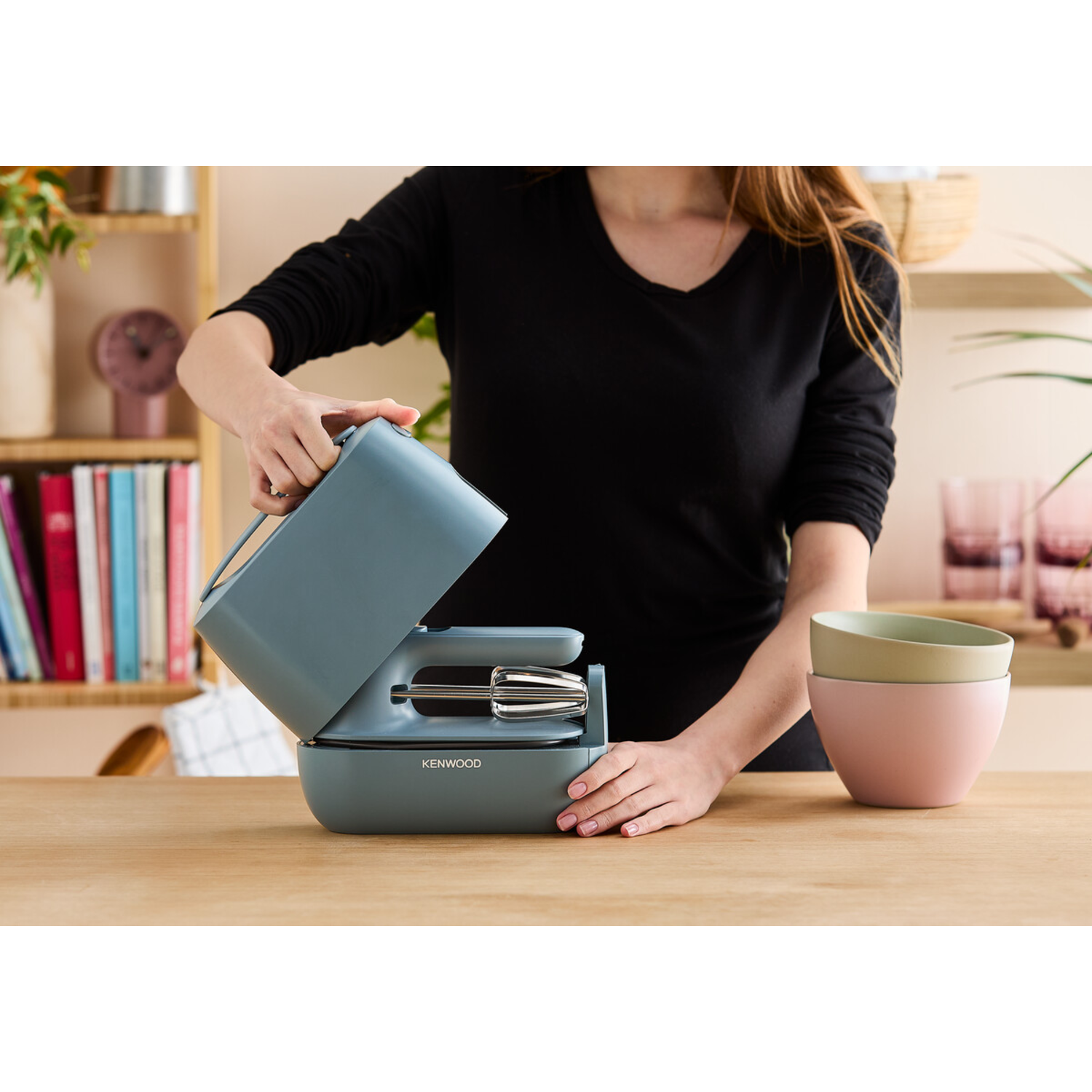 A woman assembling a blue hand mixer on a wooden table.