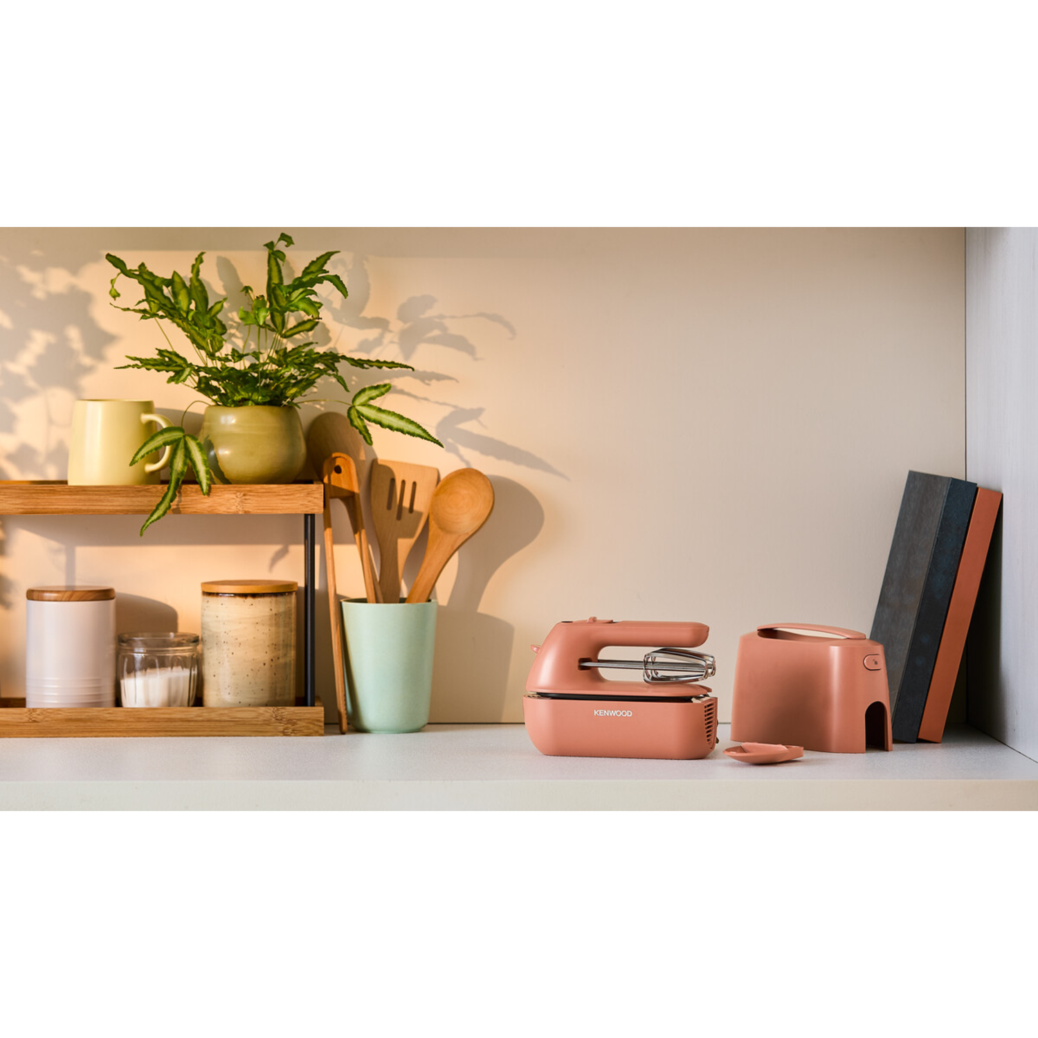 Kitchen shelf with plants, jars, wooden utensils, and pink mixer and toaster.