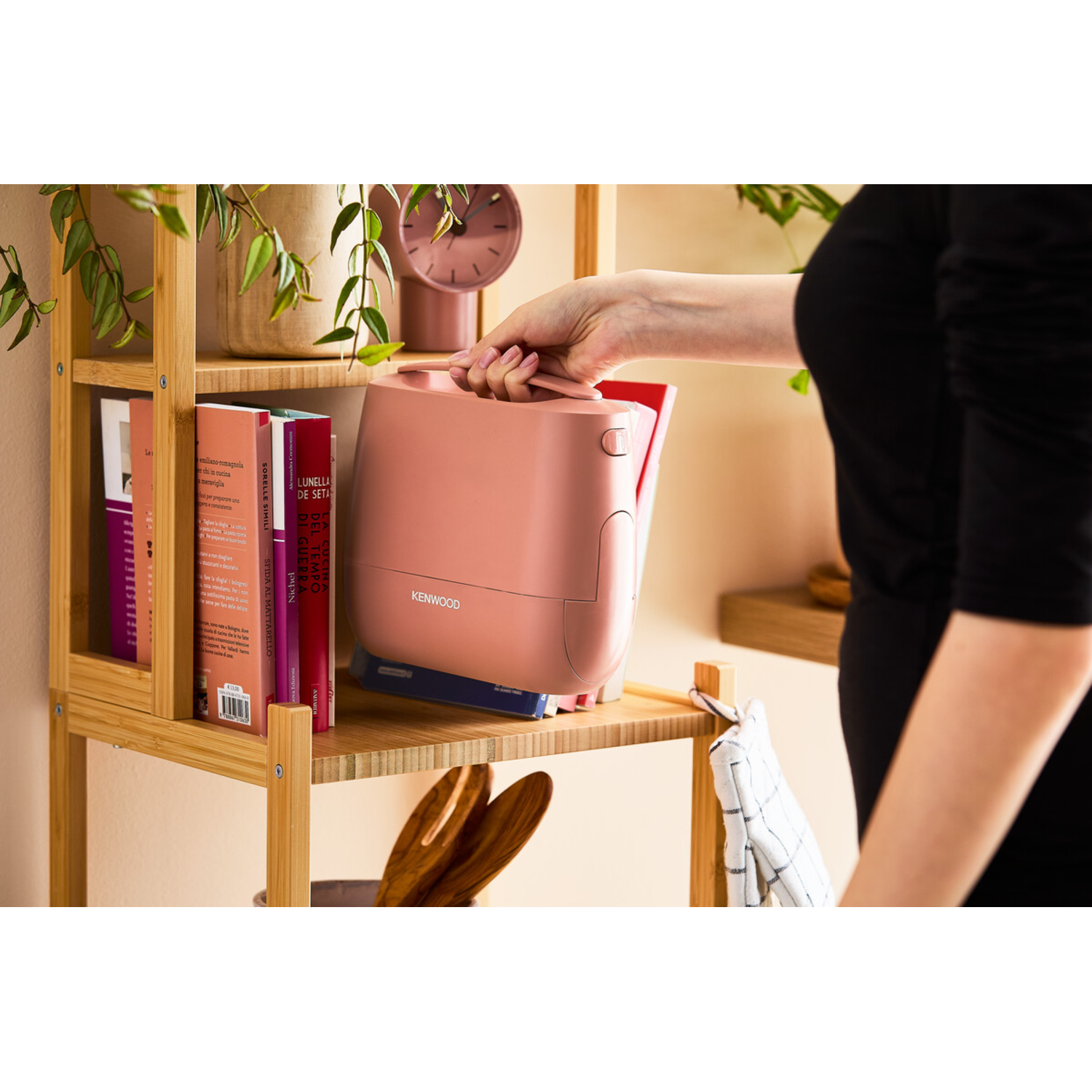 Person holding a pink Kenwood appliance on a shelf.