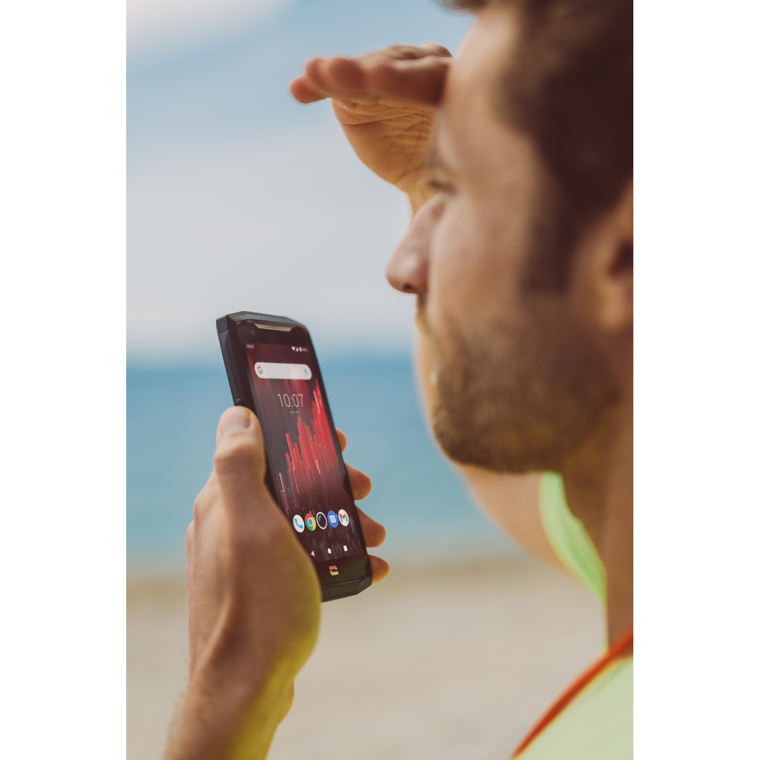 Man kijkt naar telefoonscherm op het strand. Strand en water op de achtergrond.