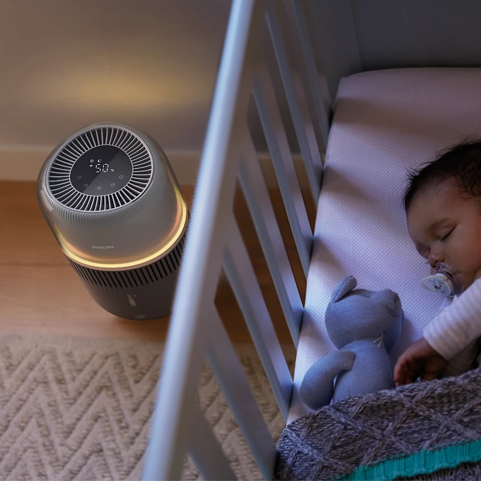 Dziecko śpiące w łóżeczku, oczyszczacz powietrza po lewej. Oczyszczacz włączony.