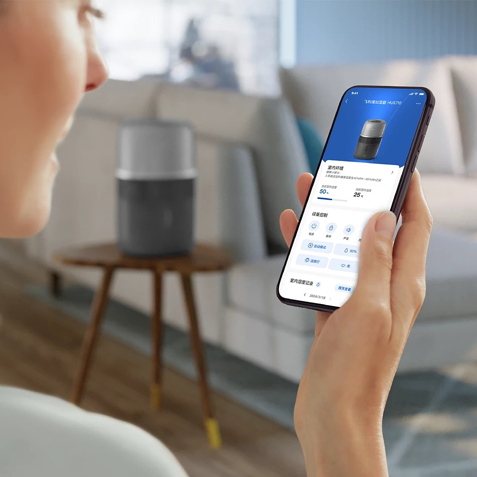 Kobieta trzyma smartfon. Ekran pokazuje aplikację sterującą czarno-srebrnym oczyszczaczem powietrza.