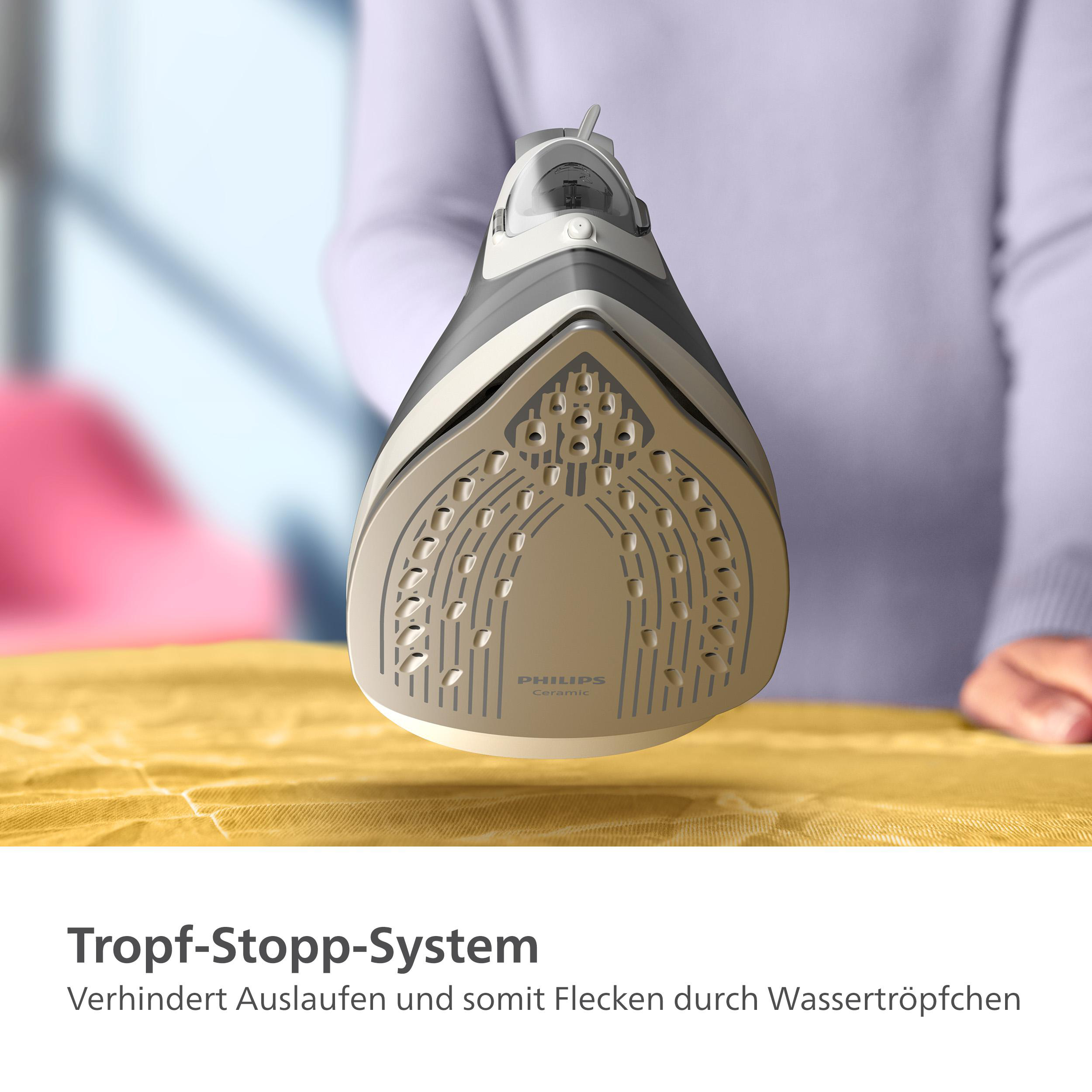 Bügeleisen, Schrägansicht, auf gelbem Stoff. Weiße und graue Farben. Frau im Hintergrund.