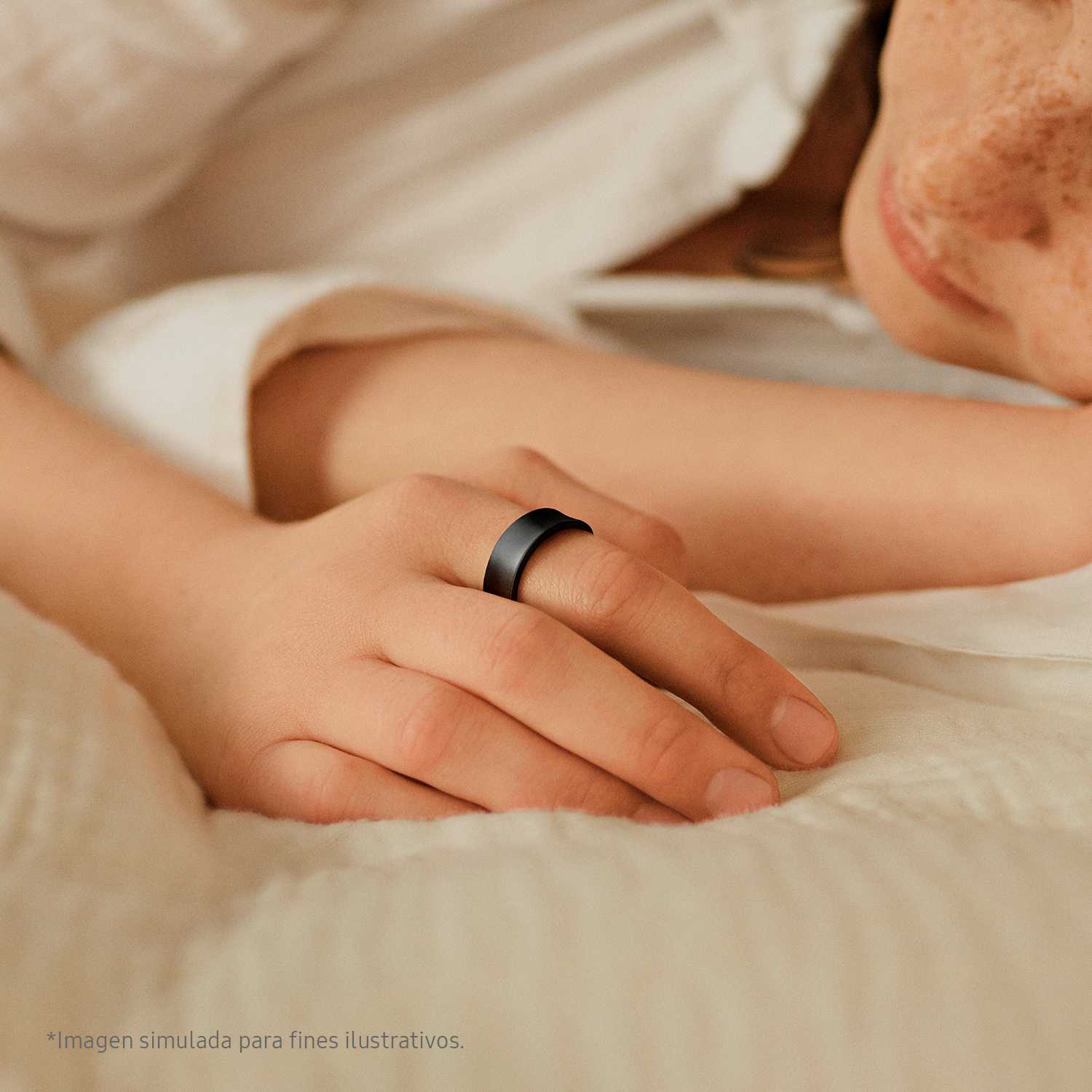 Primer plano de una mano con un anillo negro descansando sobre una cama.