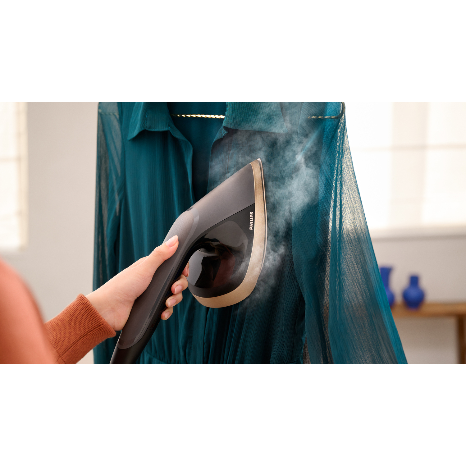 Une personne repassant une robe turquoise avec un défroisseur Philips noir et doré, avec un arrière-plan flou.