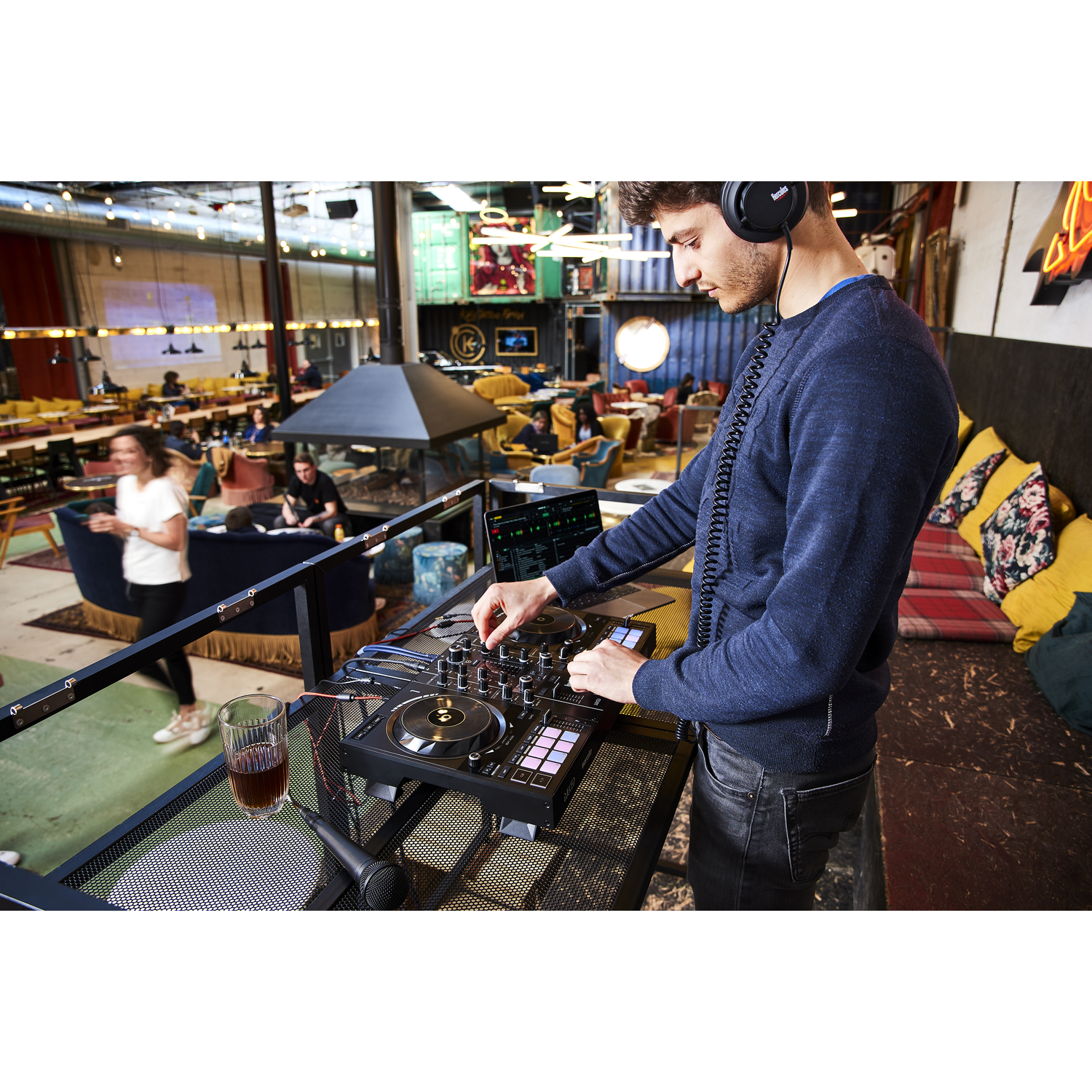 A DJ is mixing music with headphones, a mixing board, and a laptop.