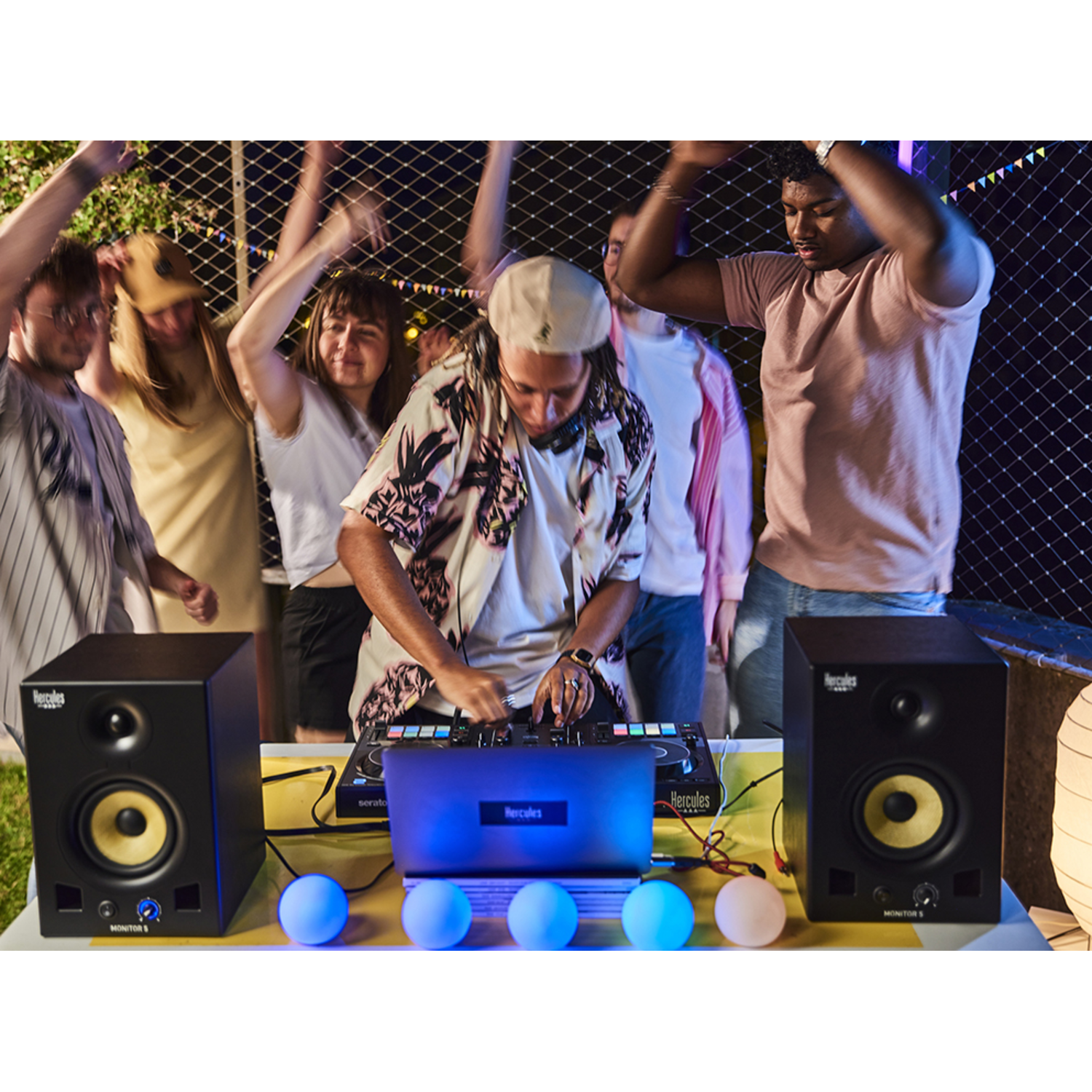 A DJ mixing music at an outdoor party with speakers and a crowd dancing.