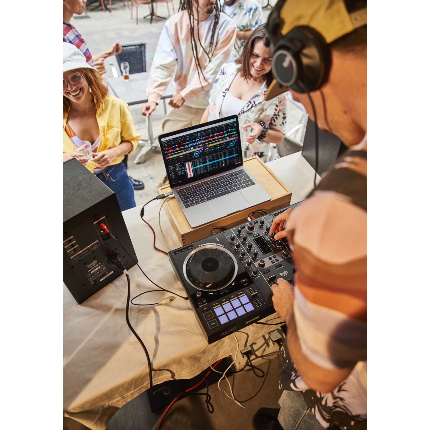 DJ at a party, using a laptop and DJ controller. Other people are dancing and enjoying themselves.