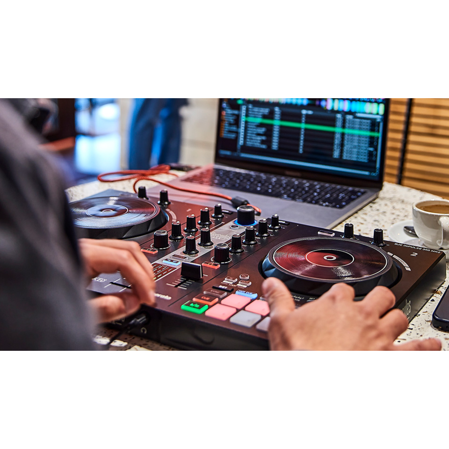 A DJ setup with turntables, mixer, and a laptop. Hands are on the mixer controls.
