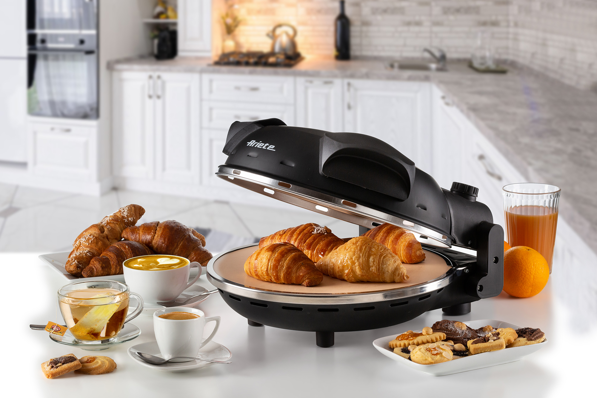 Four à pizza noir avec croissants, biscuits et boissons sur une table blanche. Arrière-plan de cuisine.