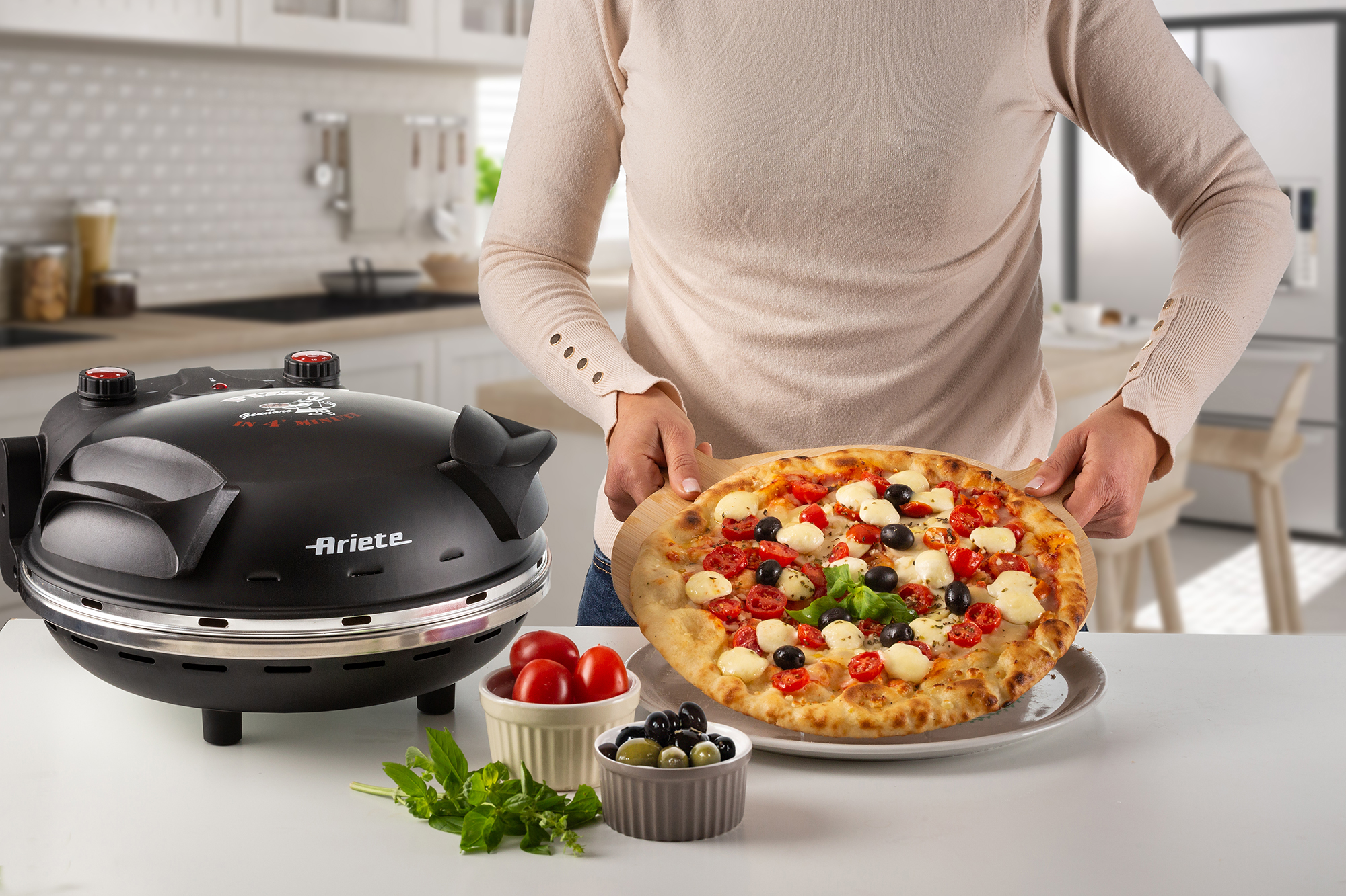 Une personne tenant une pizza avec des ingrédients frais, devant un four à pizza.