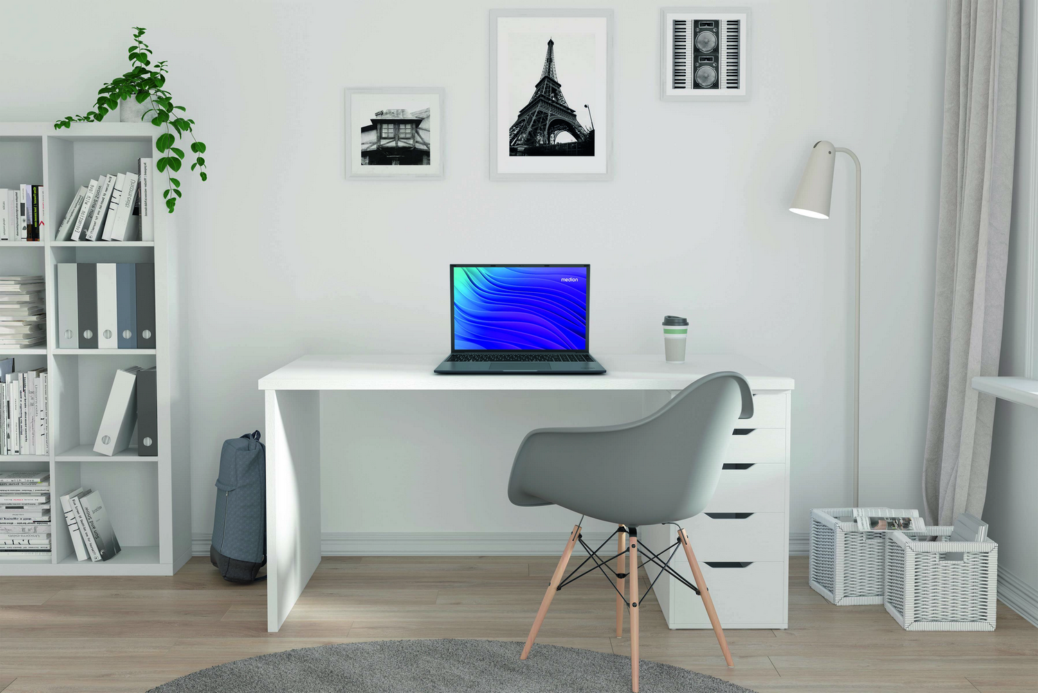 Un entorno de oficina moderno con un portátil en un escritorio blanco. Una silla gris, una estantería y cuadros enmarcado decoran la habitación.