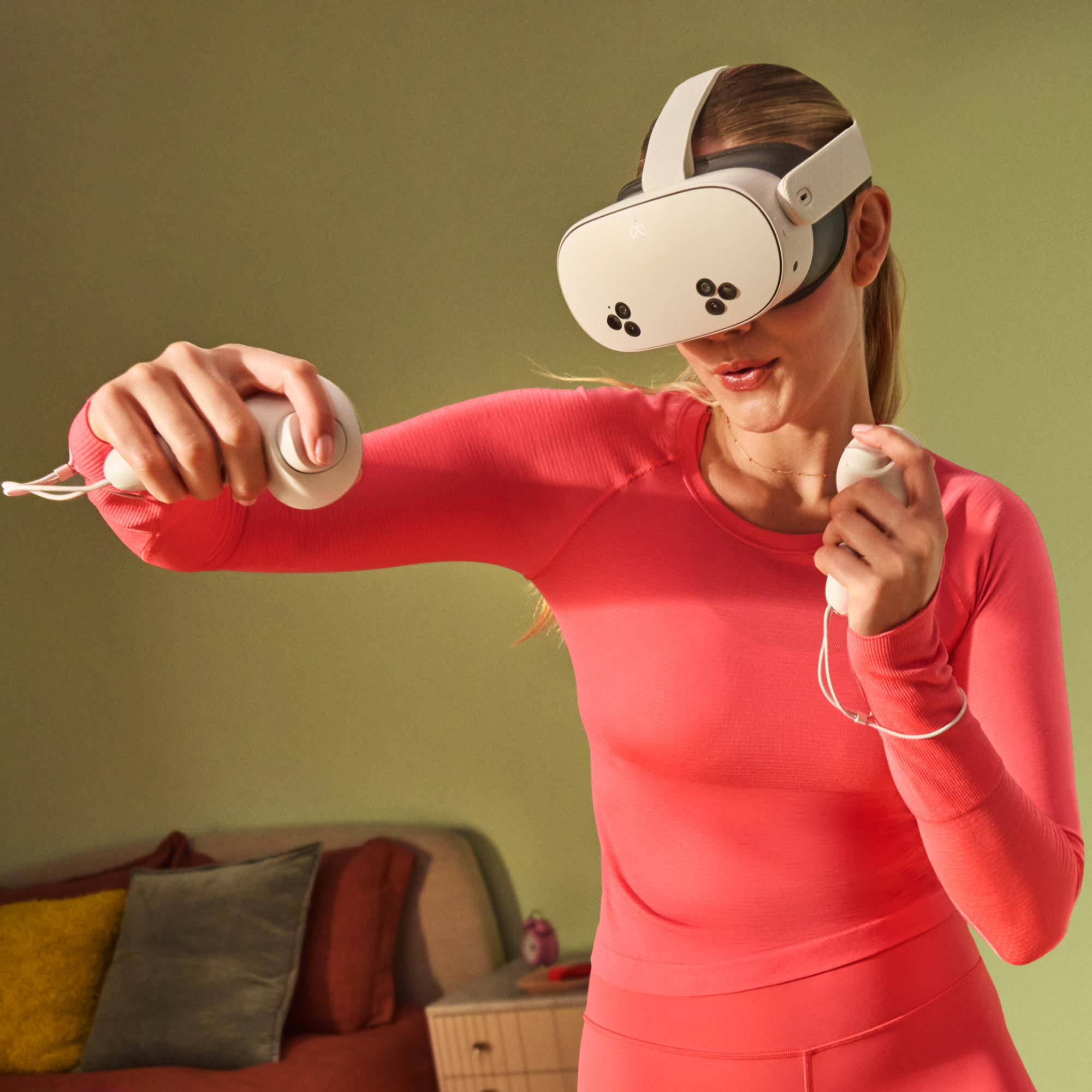 Woman in VR headset and holding controllers, arms extended, standing in a room setting.