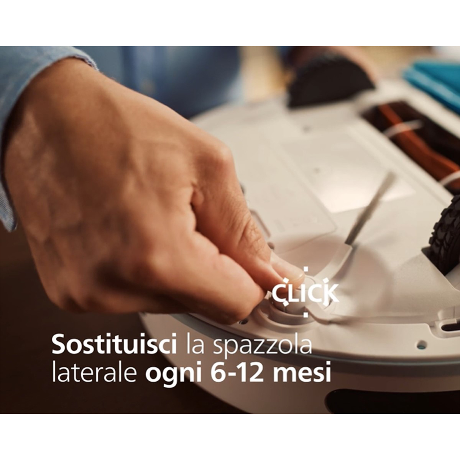 Mano di una persona che preme un pulsante 'clic' su un robot aspirapolvere, con testo in italiano.