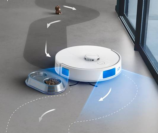Fehér robotporszívó nyíllal rajzolt útvonallal, balra egy tál étellel.