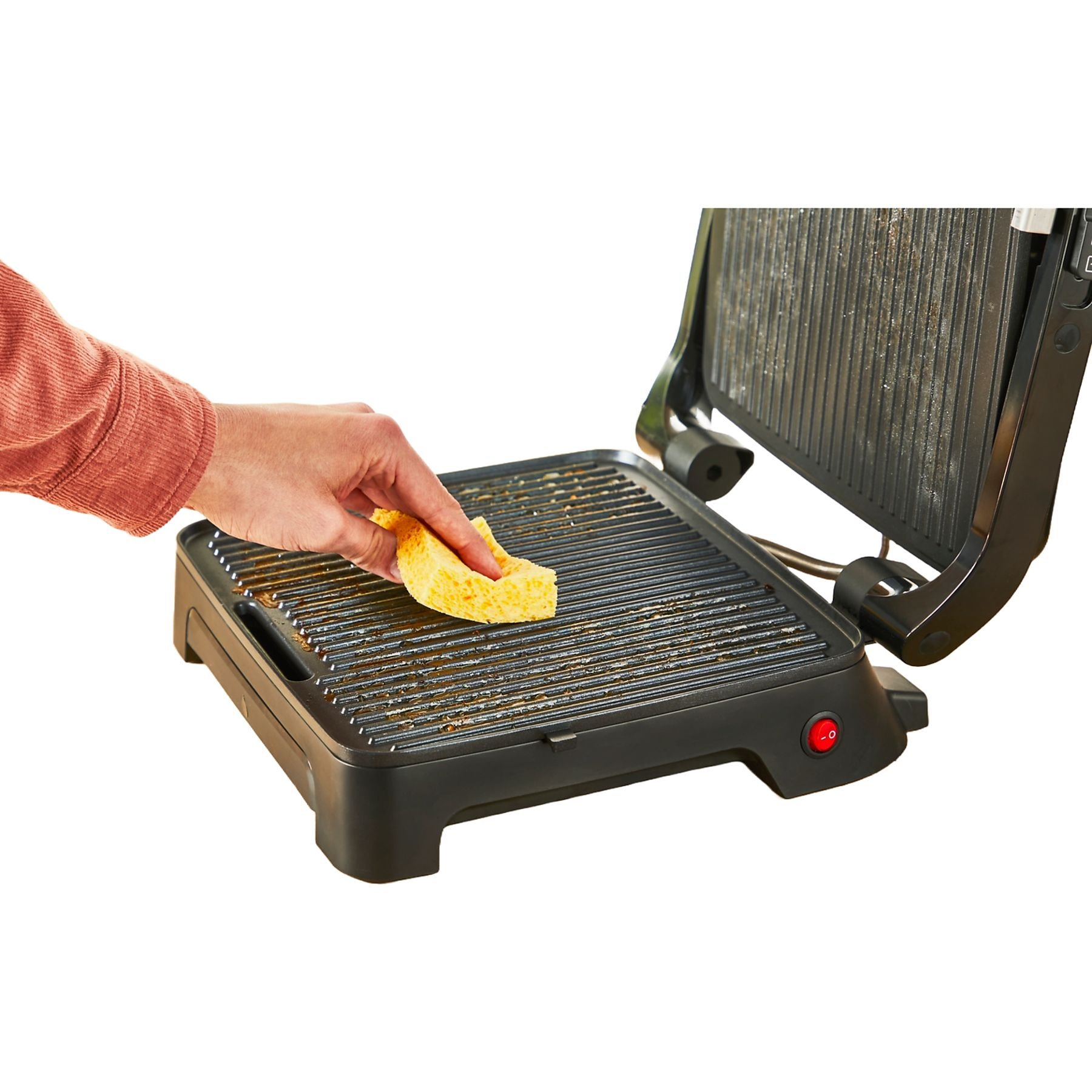 Egy személy szivaccsal tisztít egy grillt. A grill egy asztalon van, és be van kapcsolva.