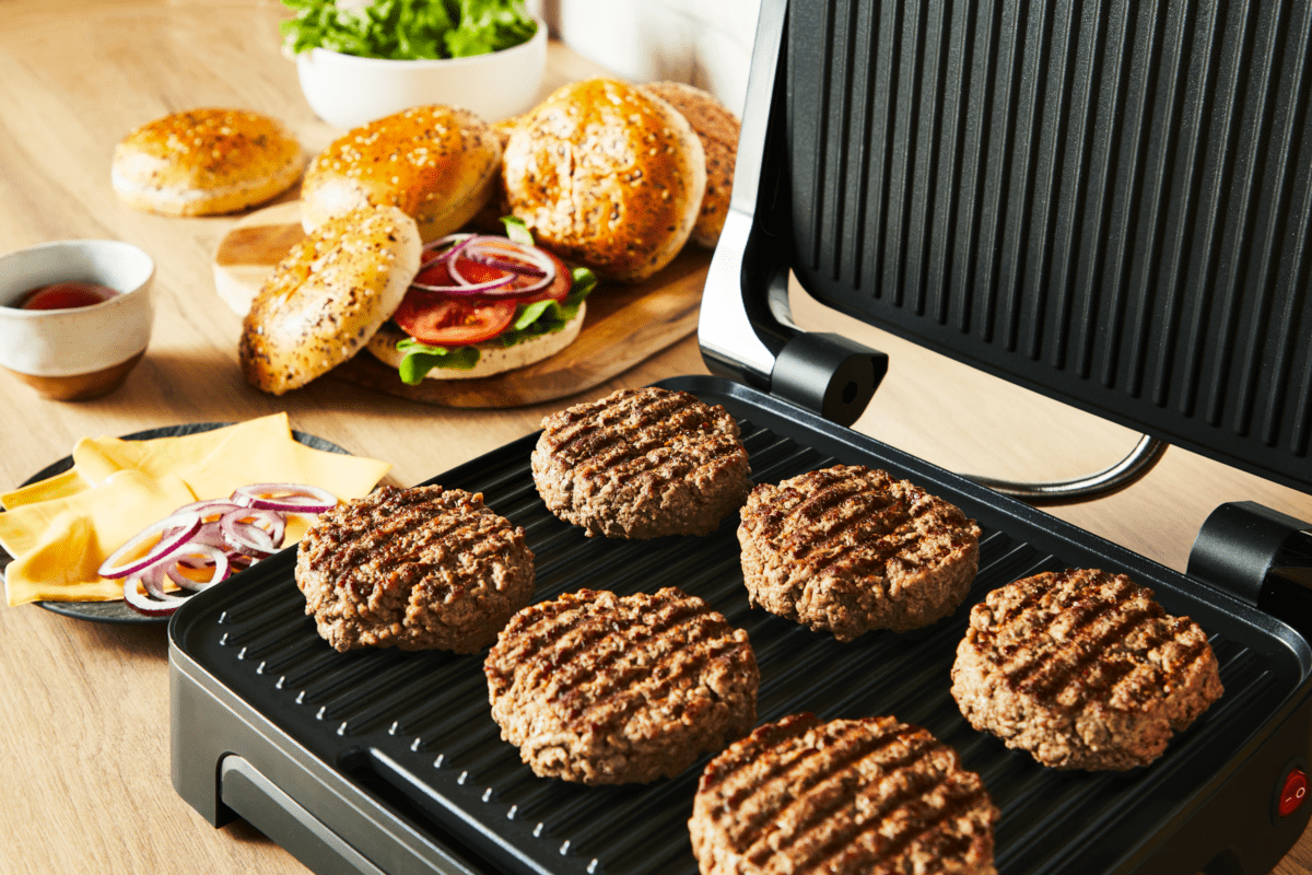Grill sült hamburgerpogácsákkal, zsemlékkel és köretekkel. Fa asztal és világos háttér.