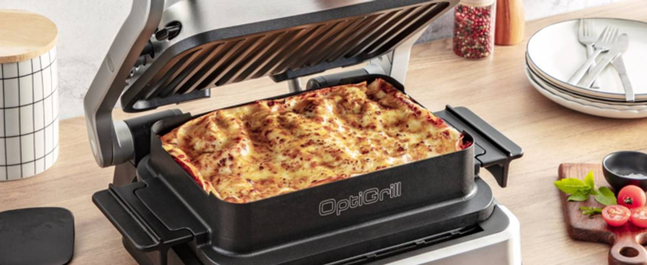 Nyitott OptiGrill sült lasagnával. A grill egy fa felületen van.