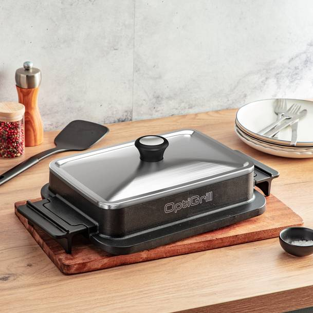 OptiGrill egy fa deszkán, zárt fedéllel. Egy fekete spatula és egy kis tálka van a közelben.