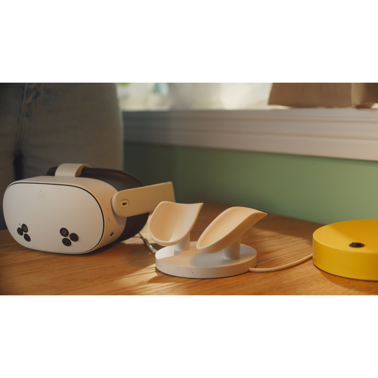 VR headset, charging stand and yellow disc on a wooden table. Background is a window and green wall.