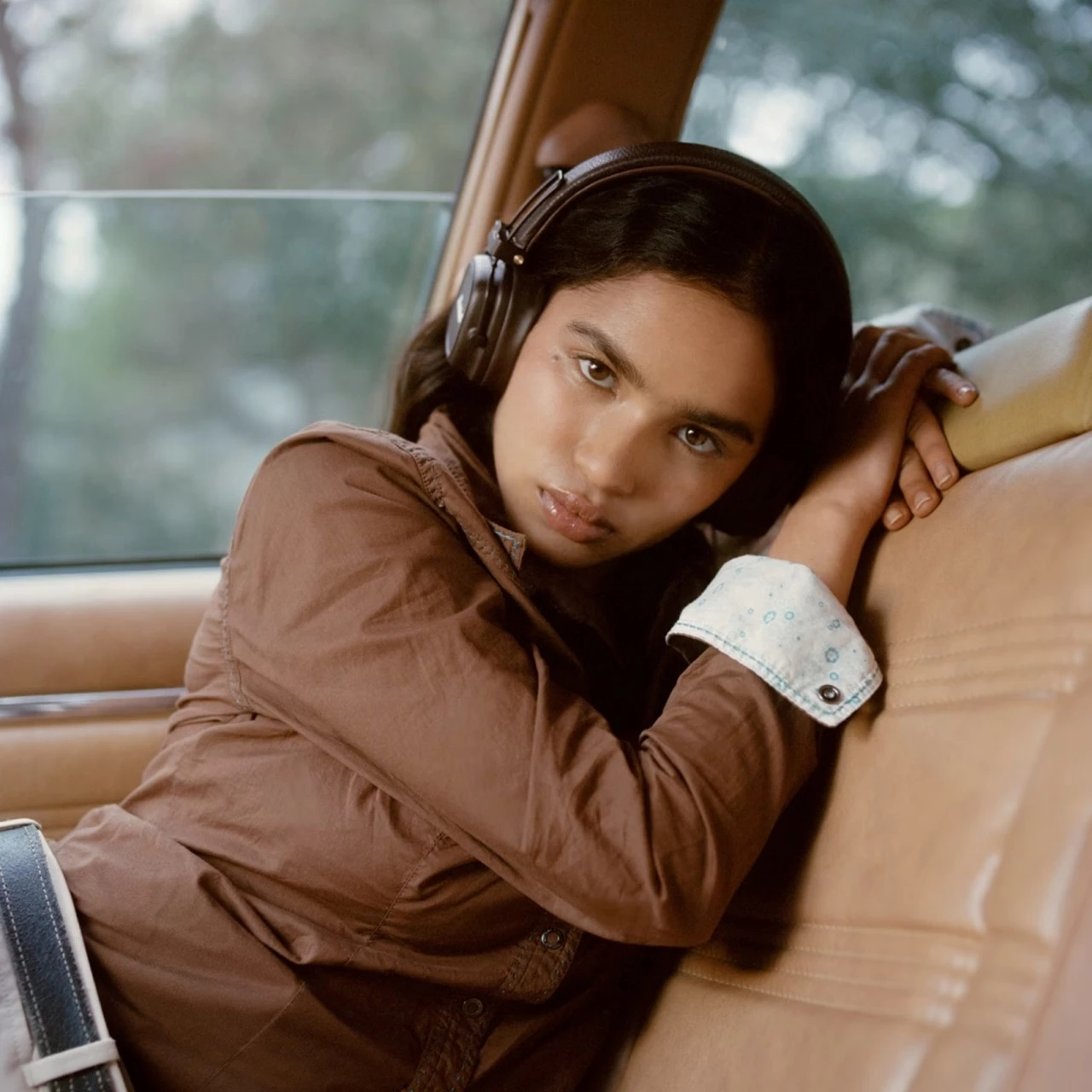 Kobieta w samochodzie w słuchawkach. Oparta na ramieniu, patrzy w kamerę.