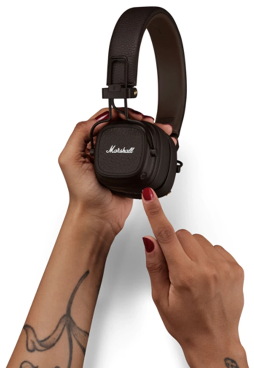 Dłonie trzymające czarne słuchawki Marshall. Czerwony lakier do paznokci na palcu wskazującym.
