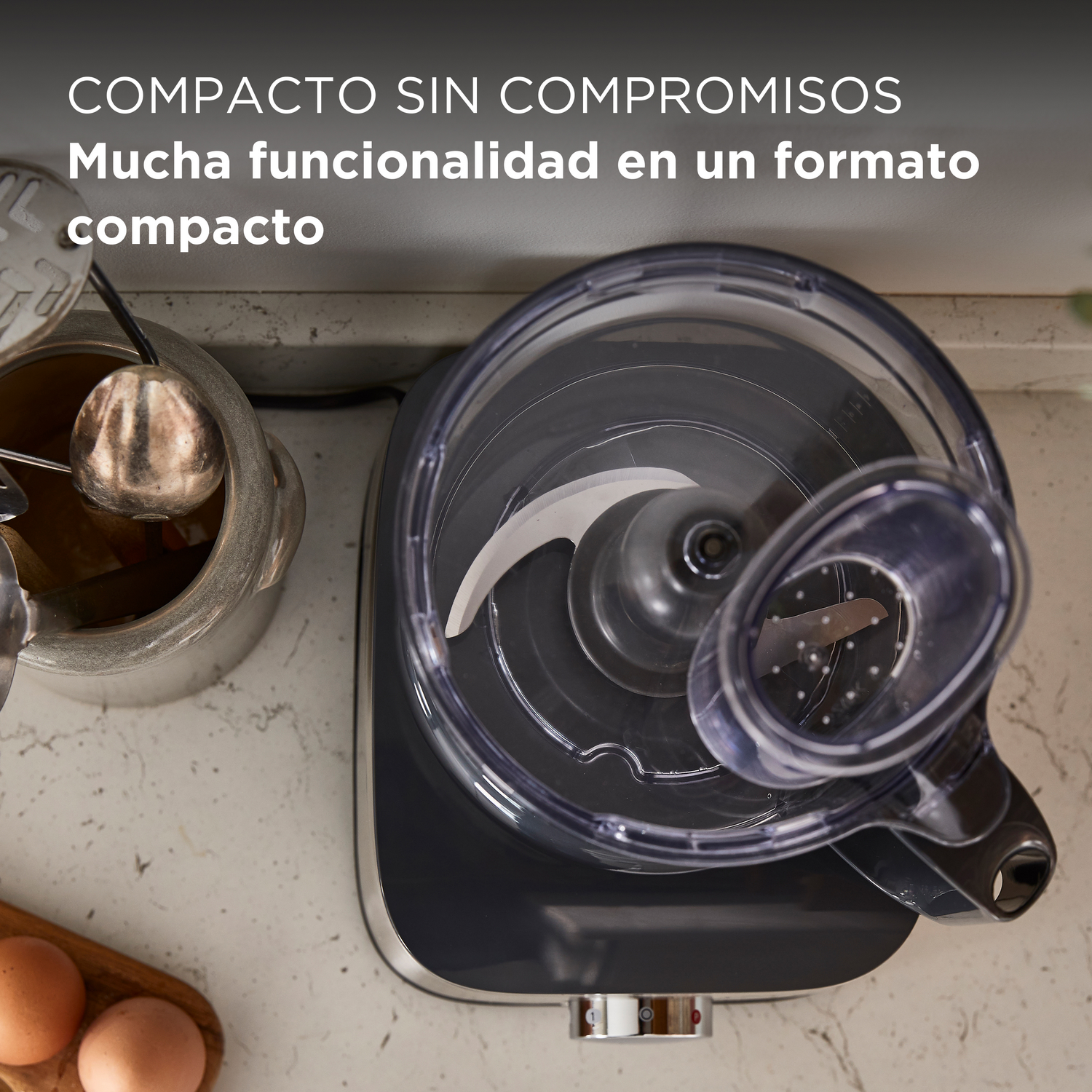 Un procesador de alimentos con un bol transparente, cuchillas y huevos en primer plano.