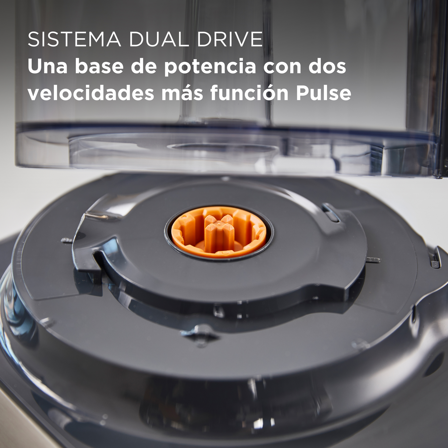 Primer plano de la base de un procesador de alimentos con un componente central naranja sobre superficie gris oscuro.