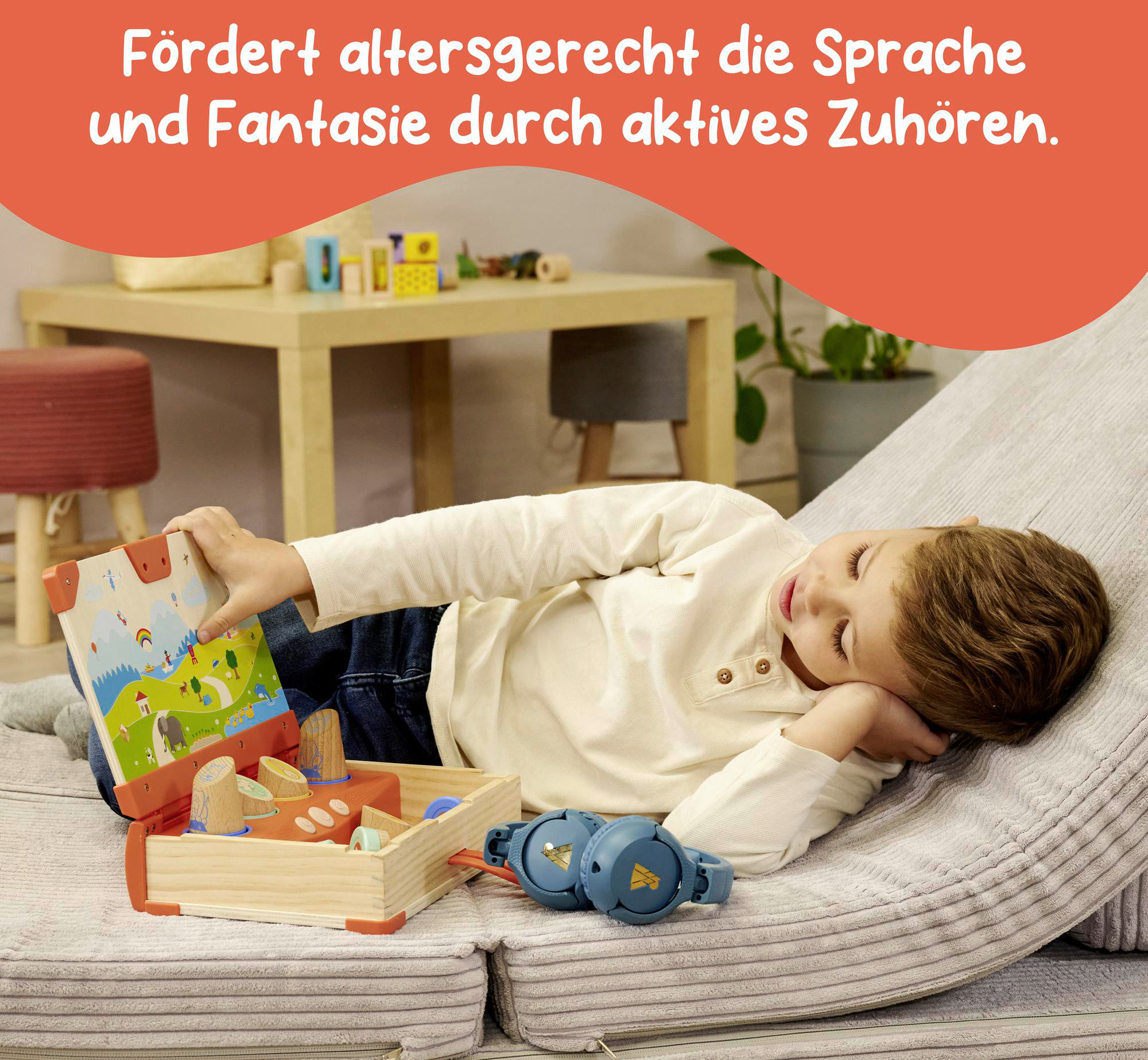 Ein Kind liegt auf einem Kissen. Es spielt mit Holzspielzeug und Kopfhörern.