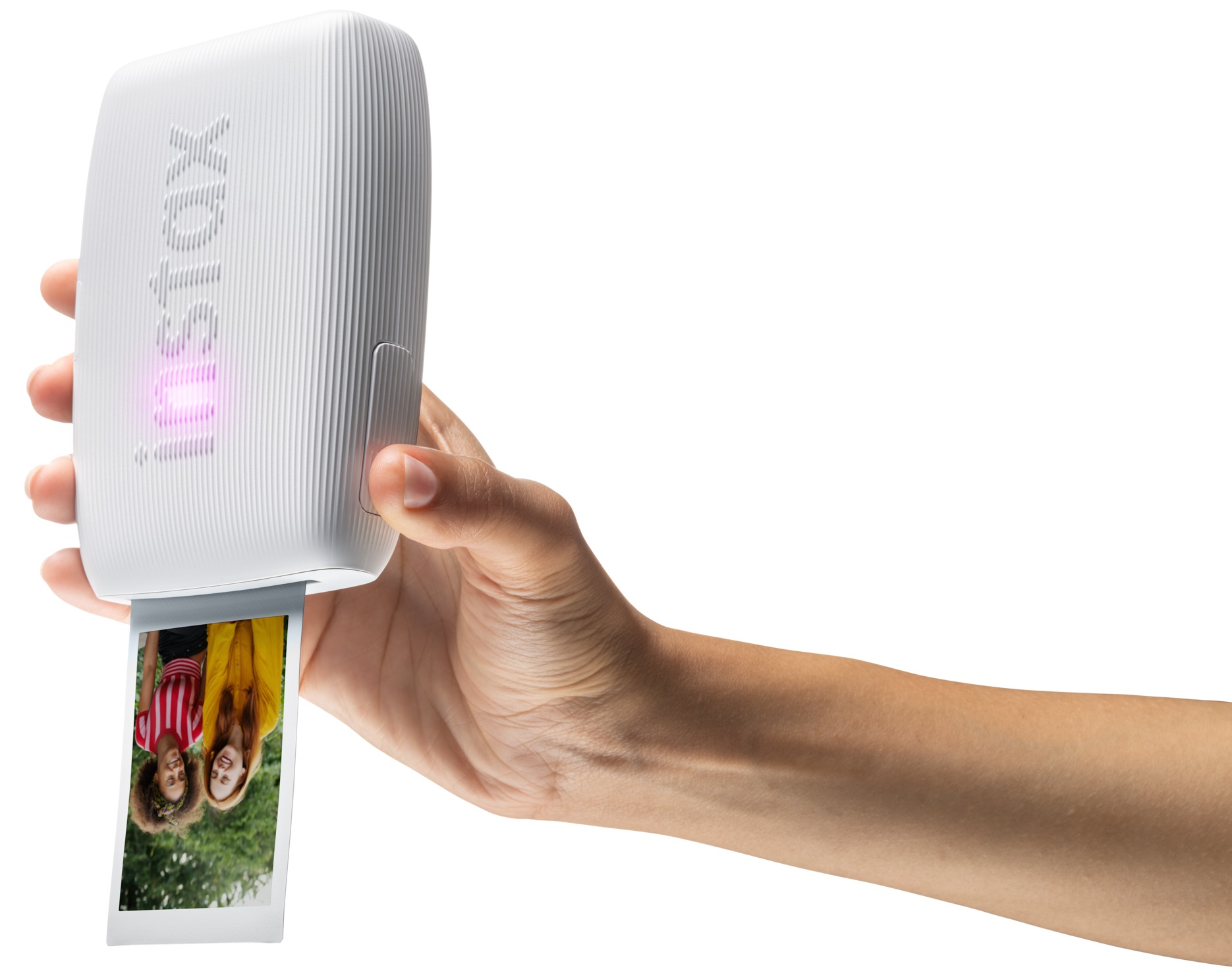 Dłoń trzyma białą drukarkę fotograficzną, drukującą zdjęcie dwóch kobiet.