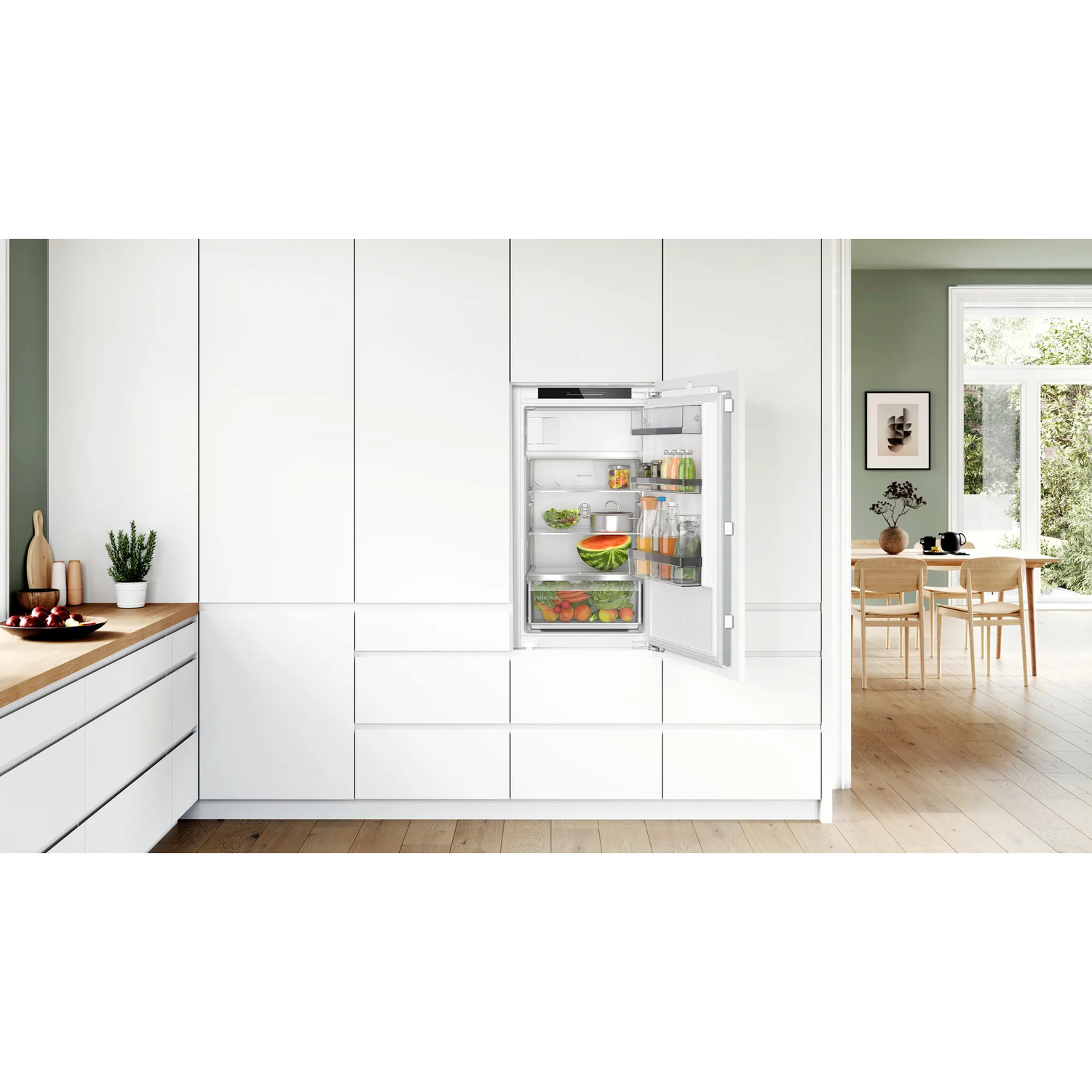Een witte koelkast, open. Binnenin fruit, groenten en drankjes. De keuken is helder.