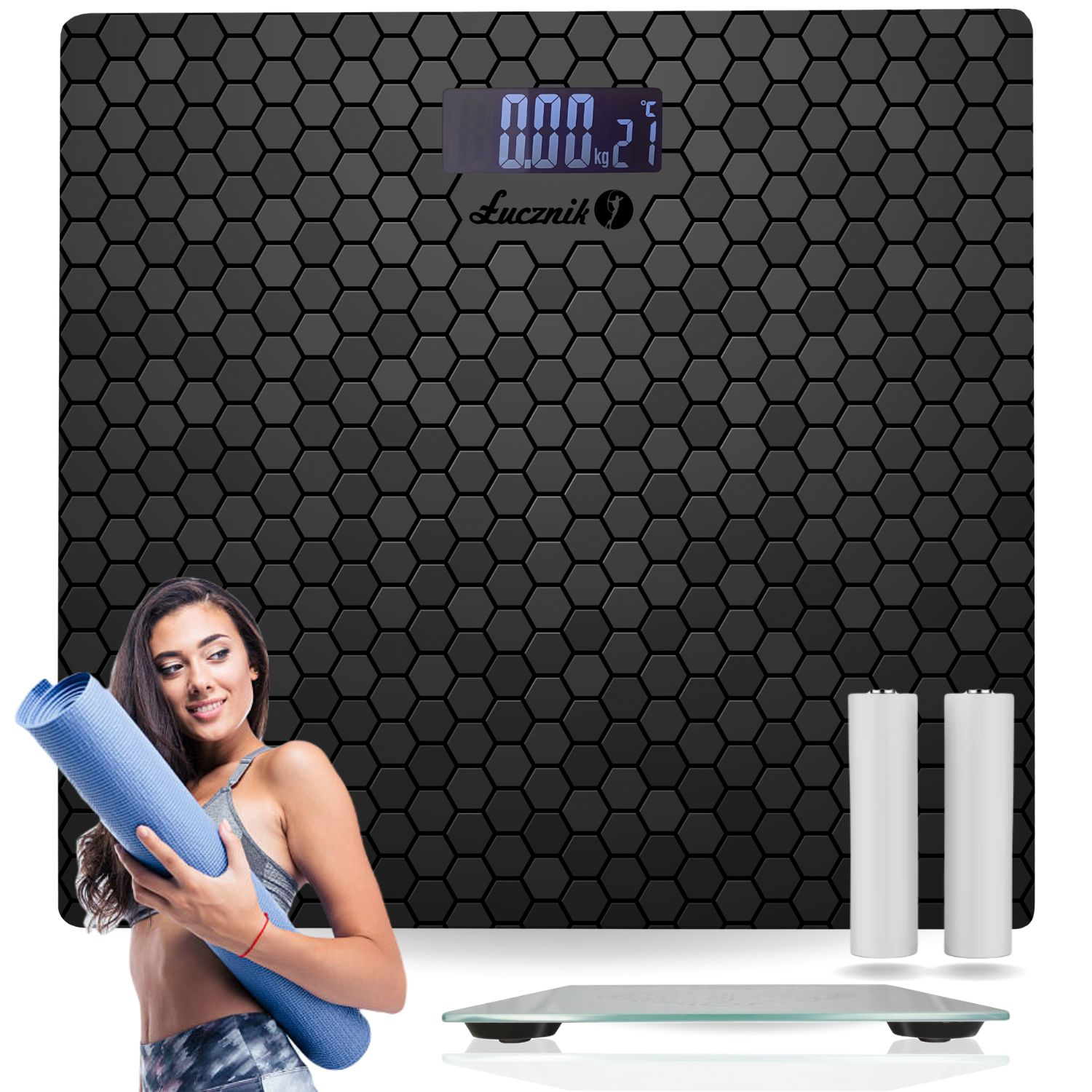 Kobieta stoi obok czarnej wagi, trzymając niebieską matę do jogi, obok dwóch białych baterii.