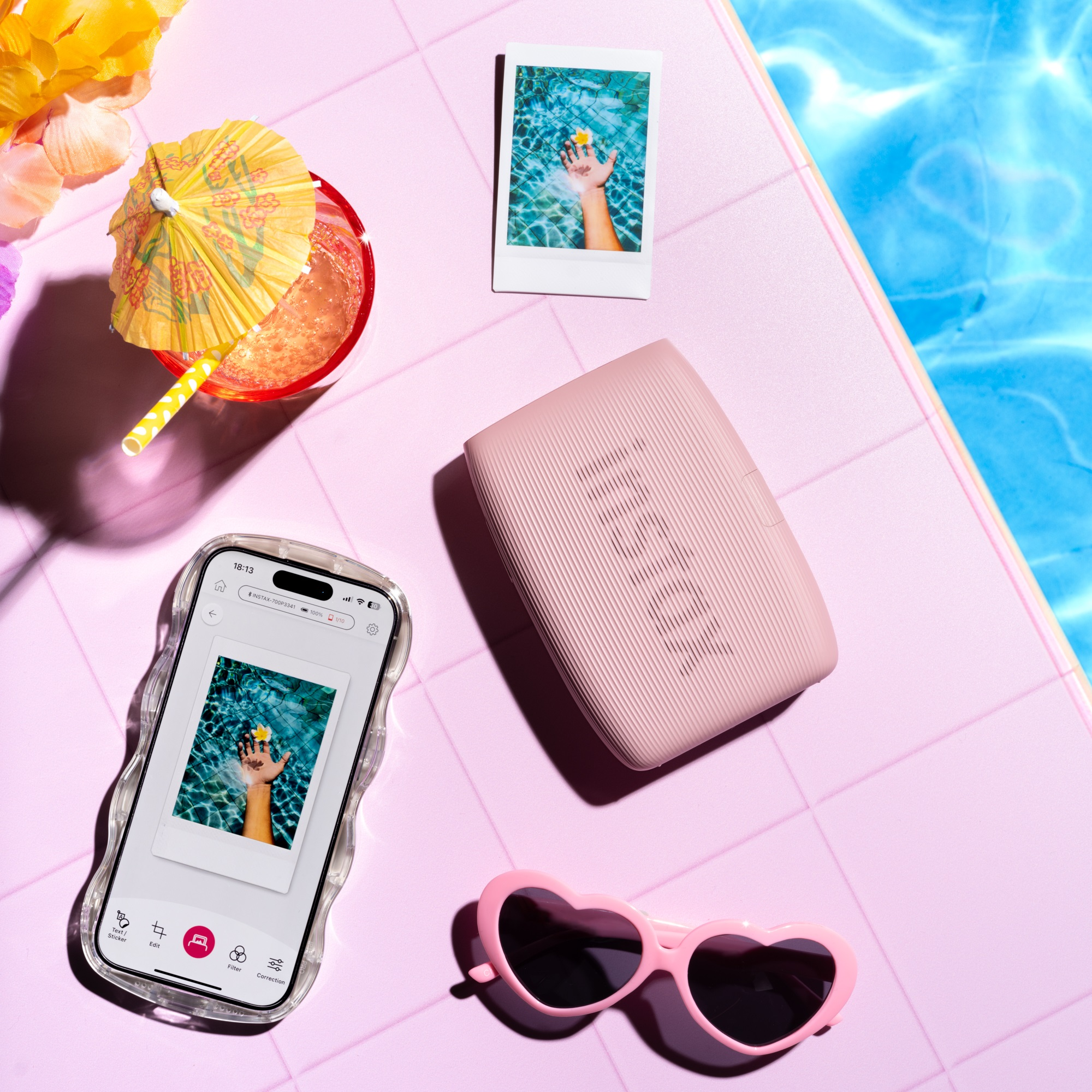 Różowy głośnik, zdjęcie polaroid, okulary przeciwsłoneczne, napój z parasolem i telefon ze zdjęciem.