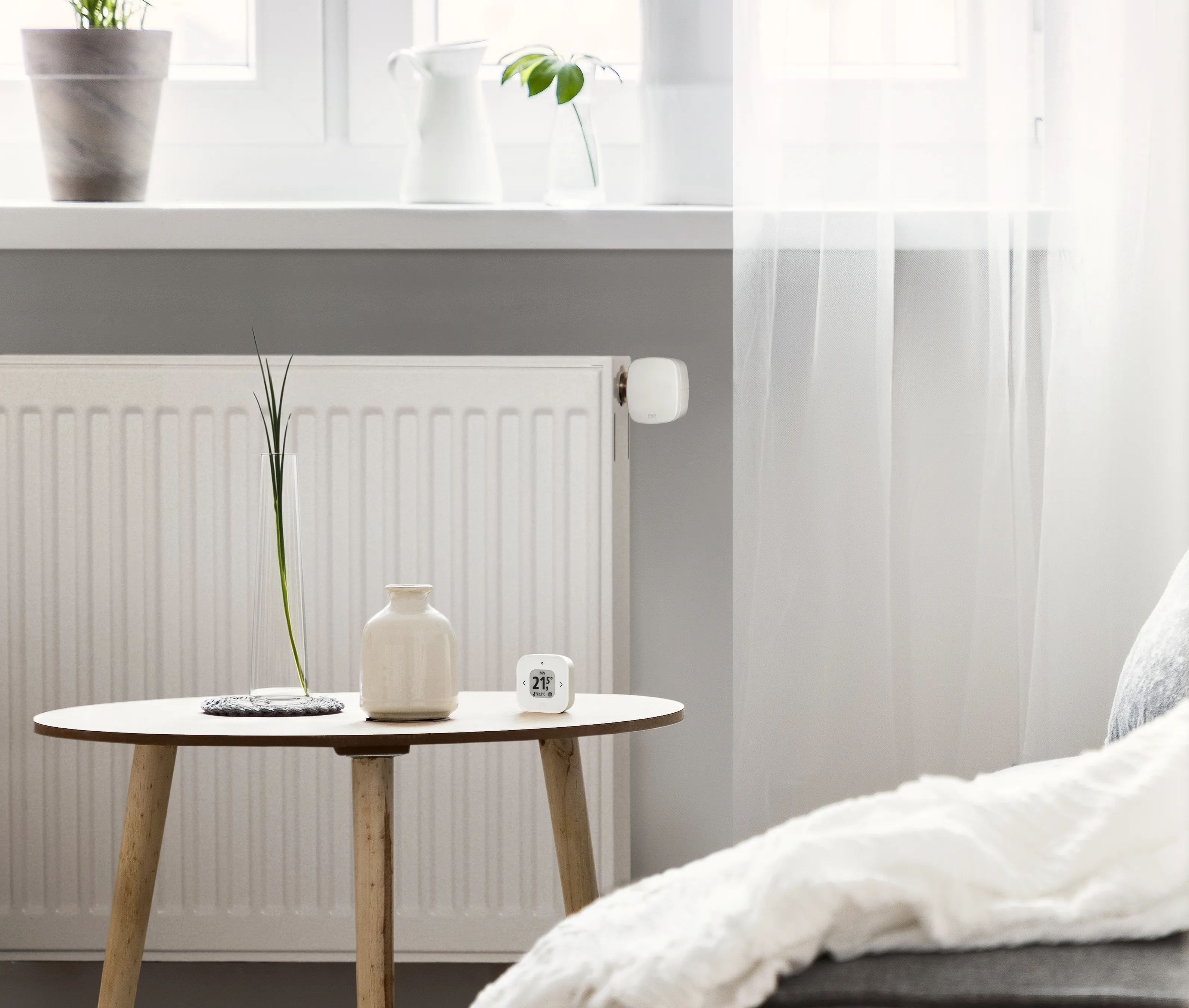 Ein Wohnzimmer mit Heizkörper, Smart-Thermostat, Tisch mit Vase und Fenster.