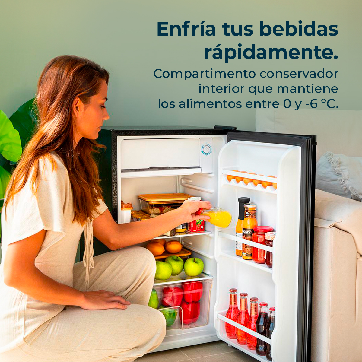 Mujer abriendo un refrigerador pequeño con frutas y bebidas dentro, en un ambiente doméstico.