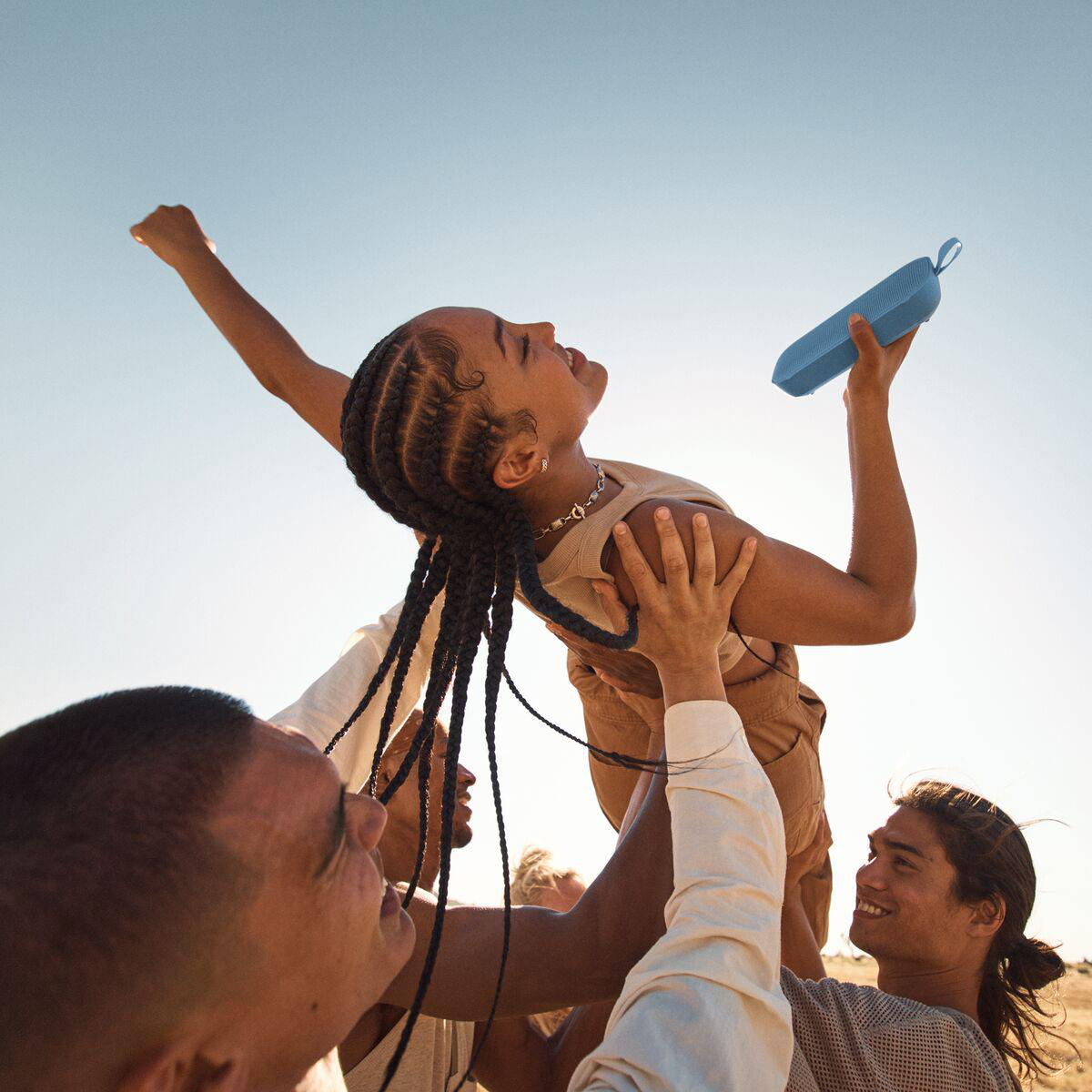 Personen halten einen blauen Lautsprecher in die Luft.