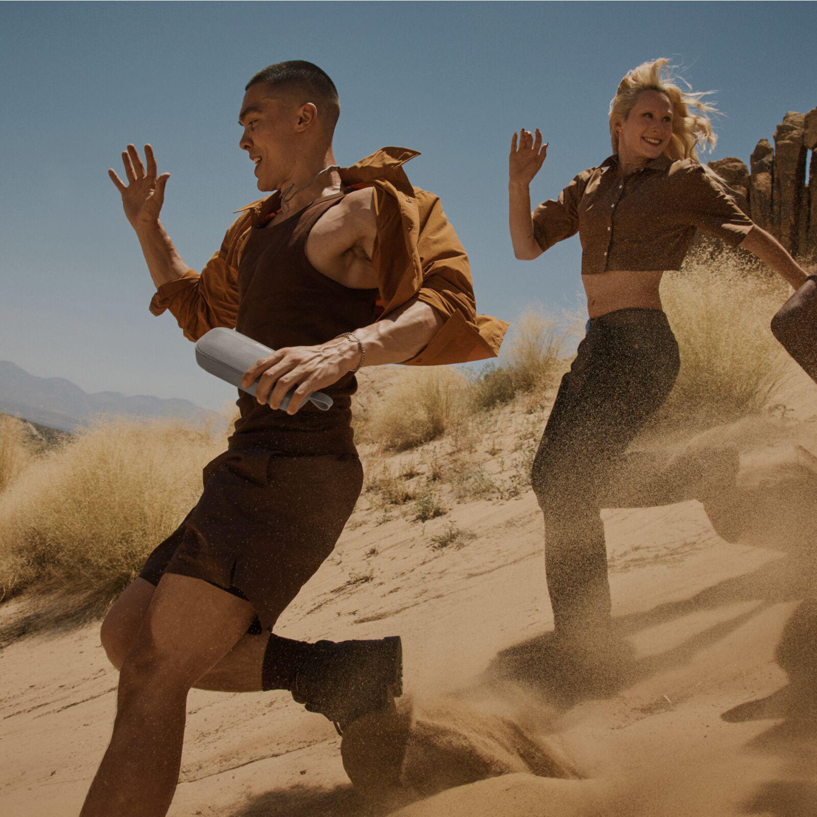 Zwei Personen rennen in einer Wüste, eine hält einen Lautsprecher.