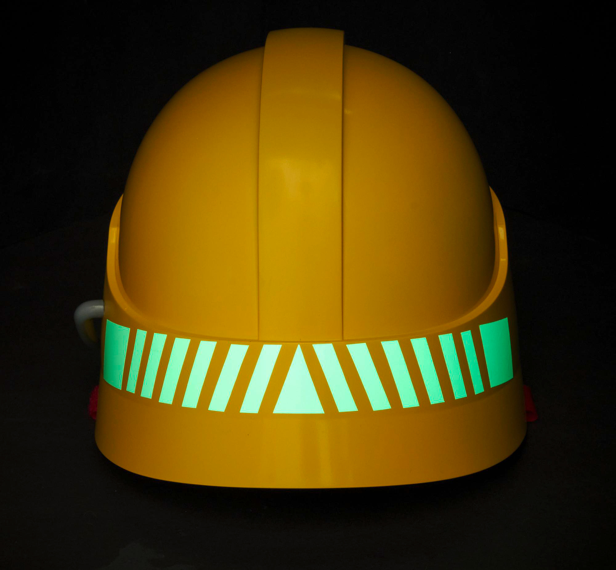 Ein gelber Bauhelm mit einem reflektierenden grünen Band. Er befindet sich auf schwarzem Hintergrund.