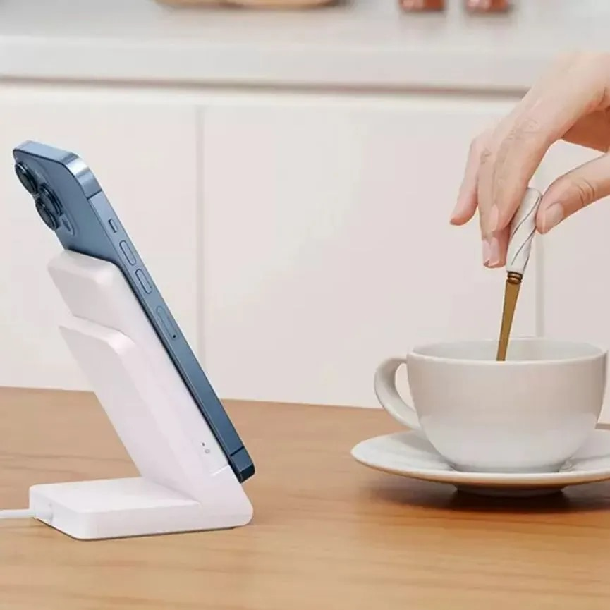 Beyaz şarj cihazında telefon. El, fincana kahve döken kaşıkla.