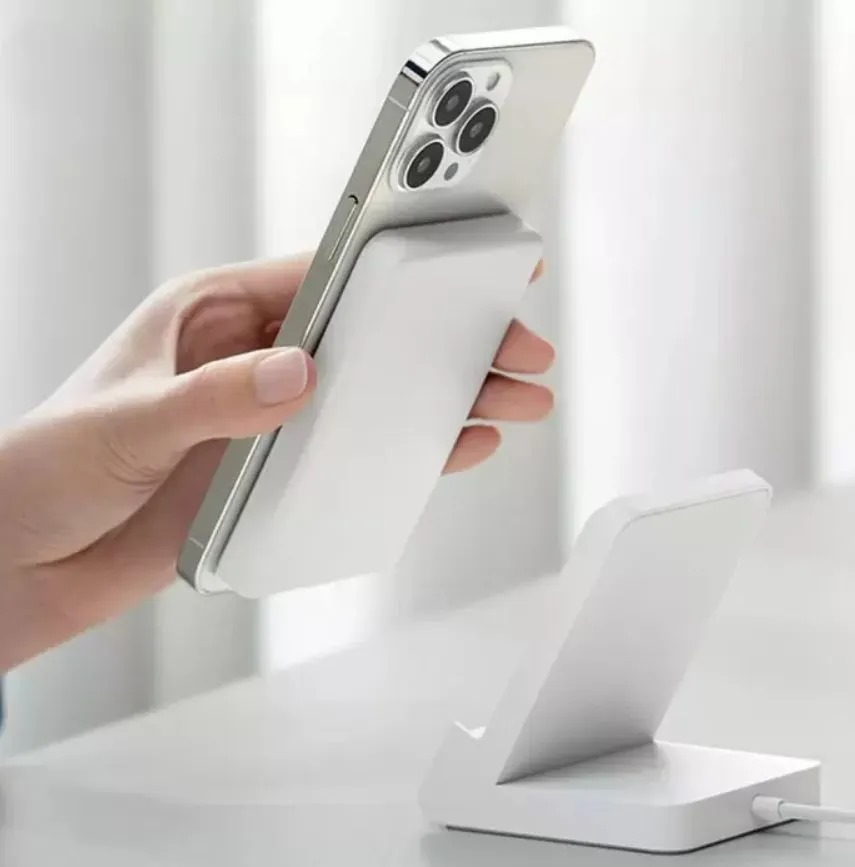 Bir el, beyaz bir şarj standının üzerinde beyaz bir telefon tutuyor. Telefon beyaz bir şarj panosuna bağlı.