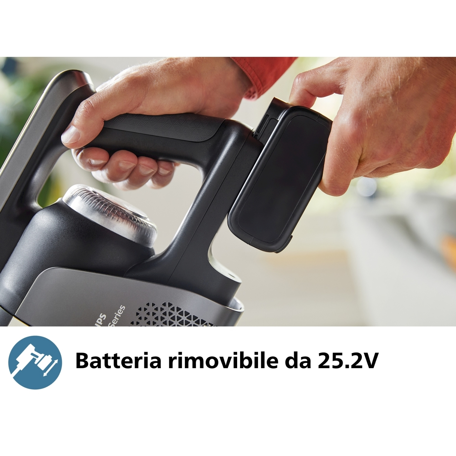 Le mani di una persona stanno rimuovendo una batteria nera da un aspirapolvere senza fili. Lo sfondo è sfocato.