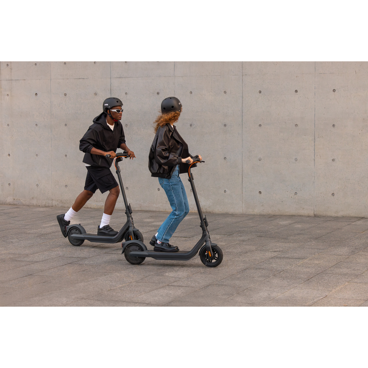 Deux personnes en scooter, l'une en noir, l'autre en veste noire, dans une rue de la ville.